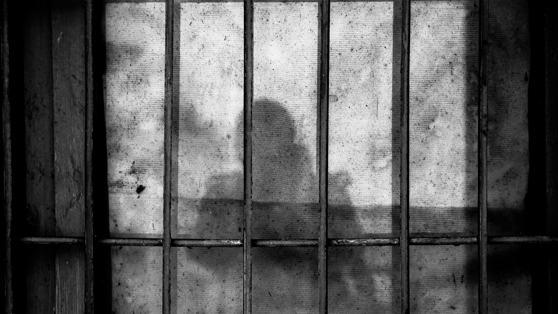 a shadow of a person behind bars in a jail cell
