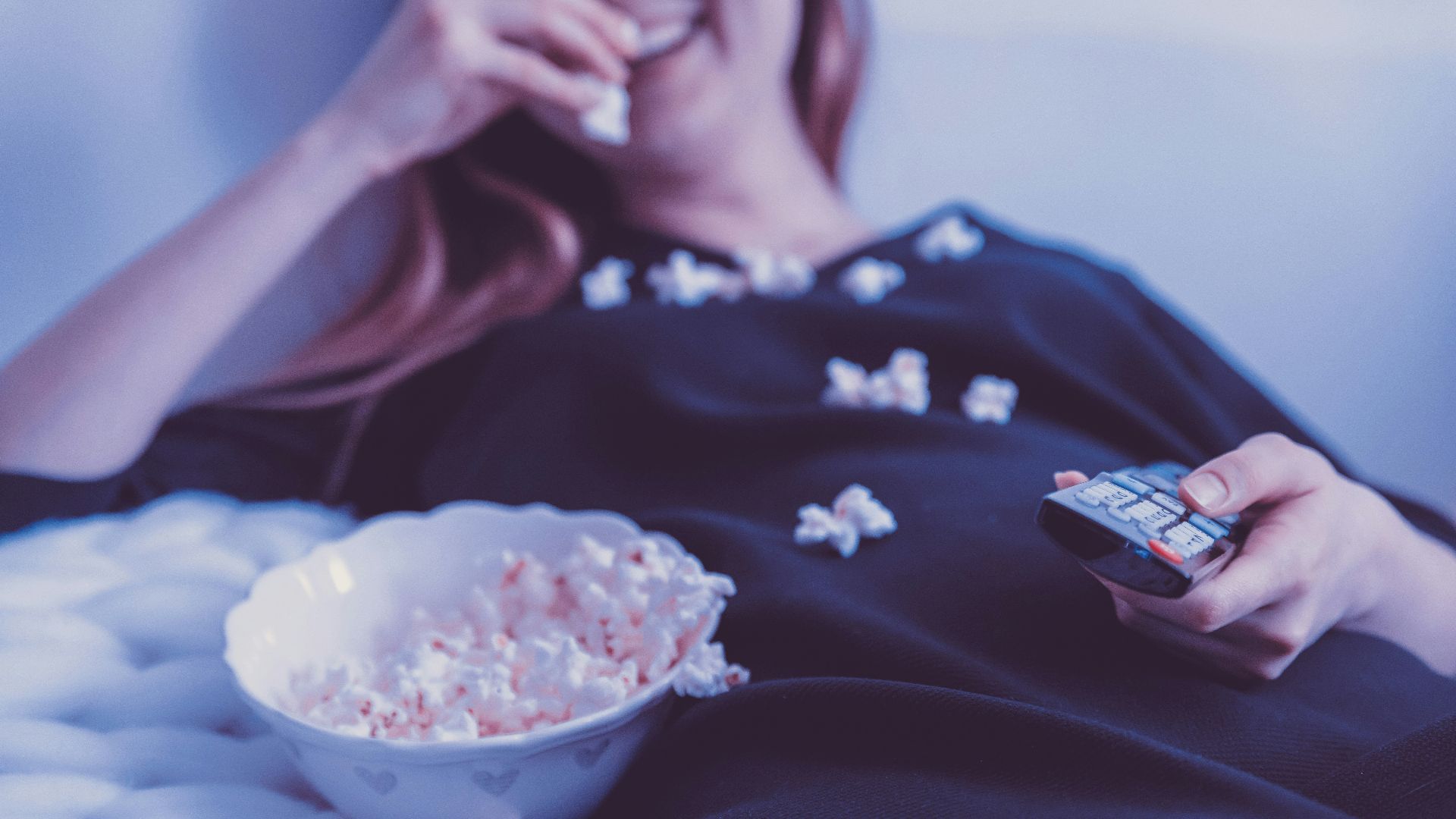 woman lying on bed while eating puff corn