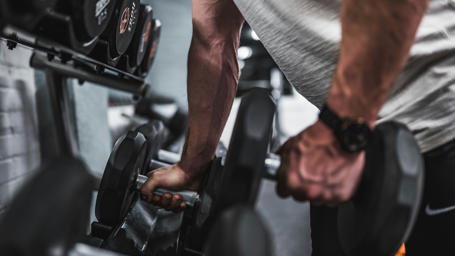 person in gray shirt holding black dumbbell