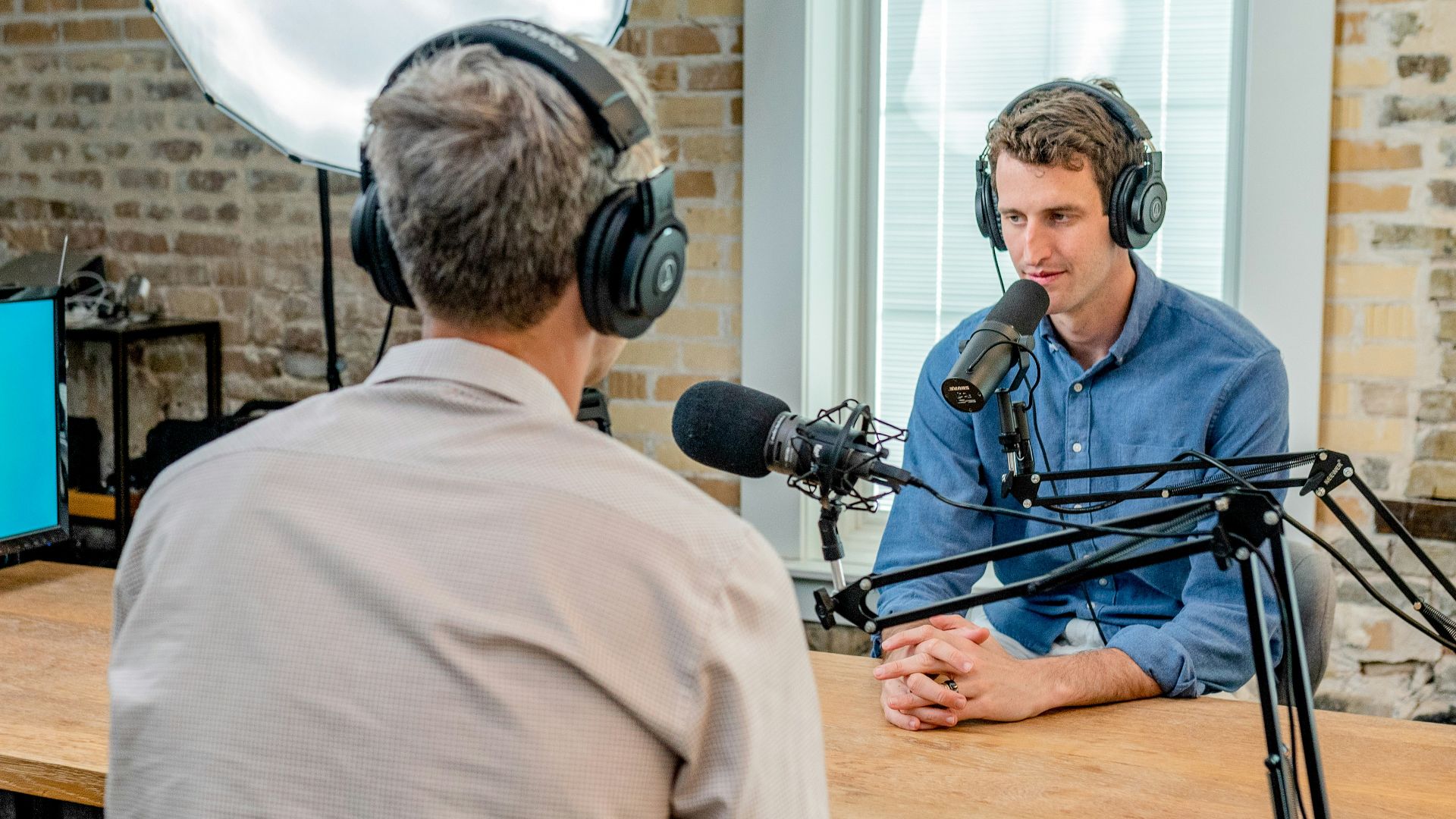 man in gray shirt leaning on table with headphones facing another man leaning on table with headboard