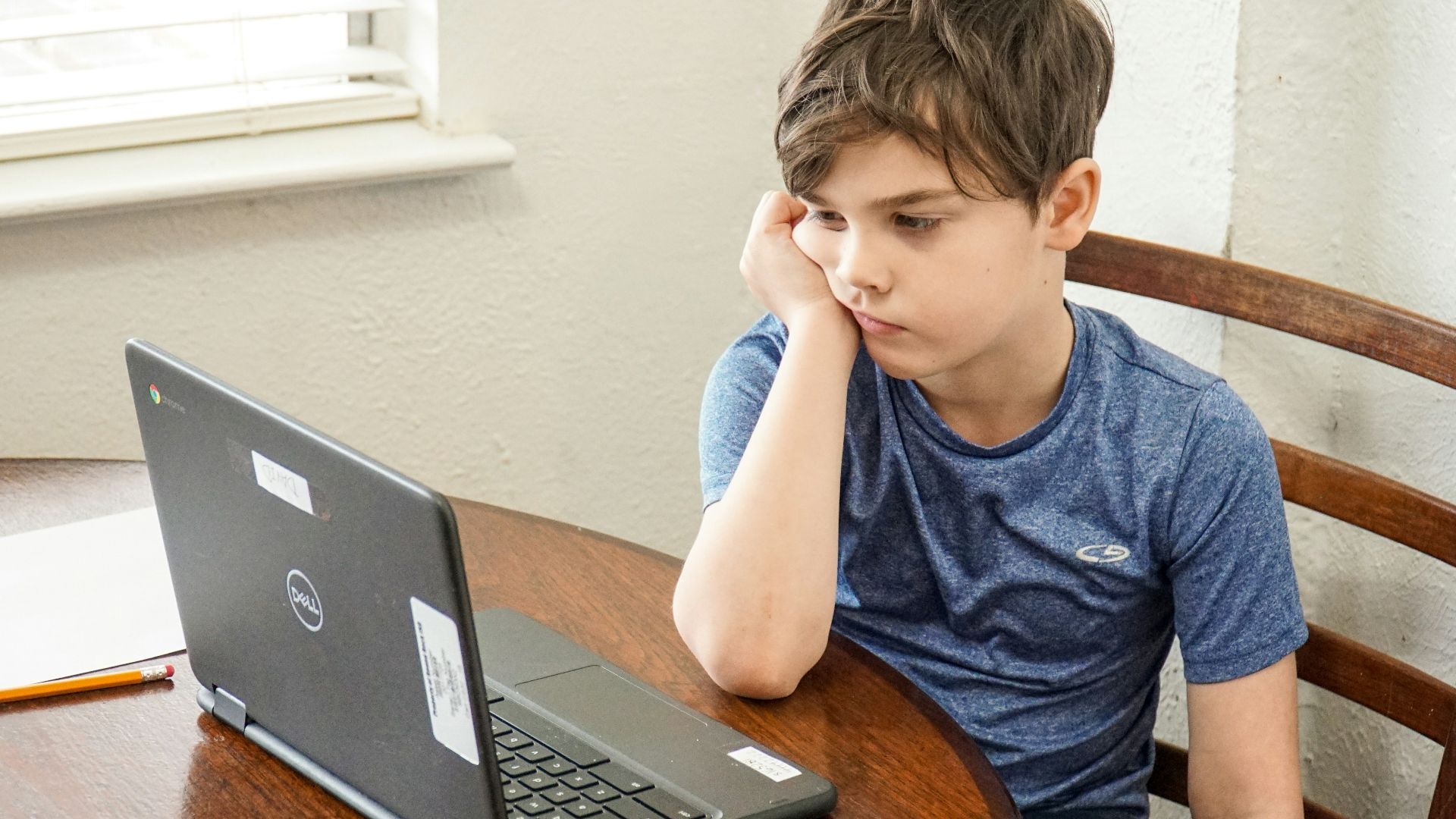 boy in blue crew neck t-shirt using macbook pro on brown wooden table