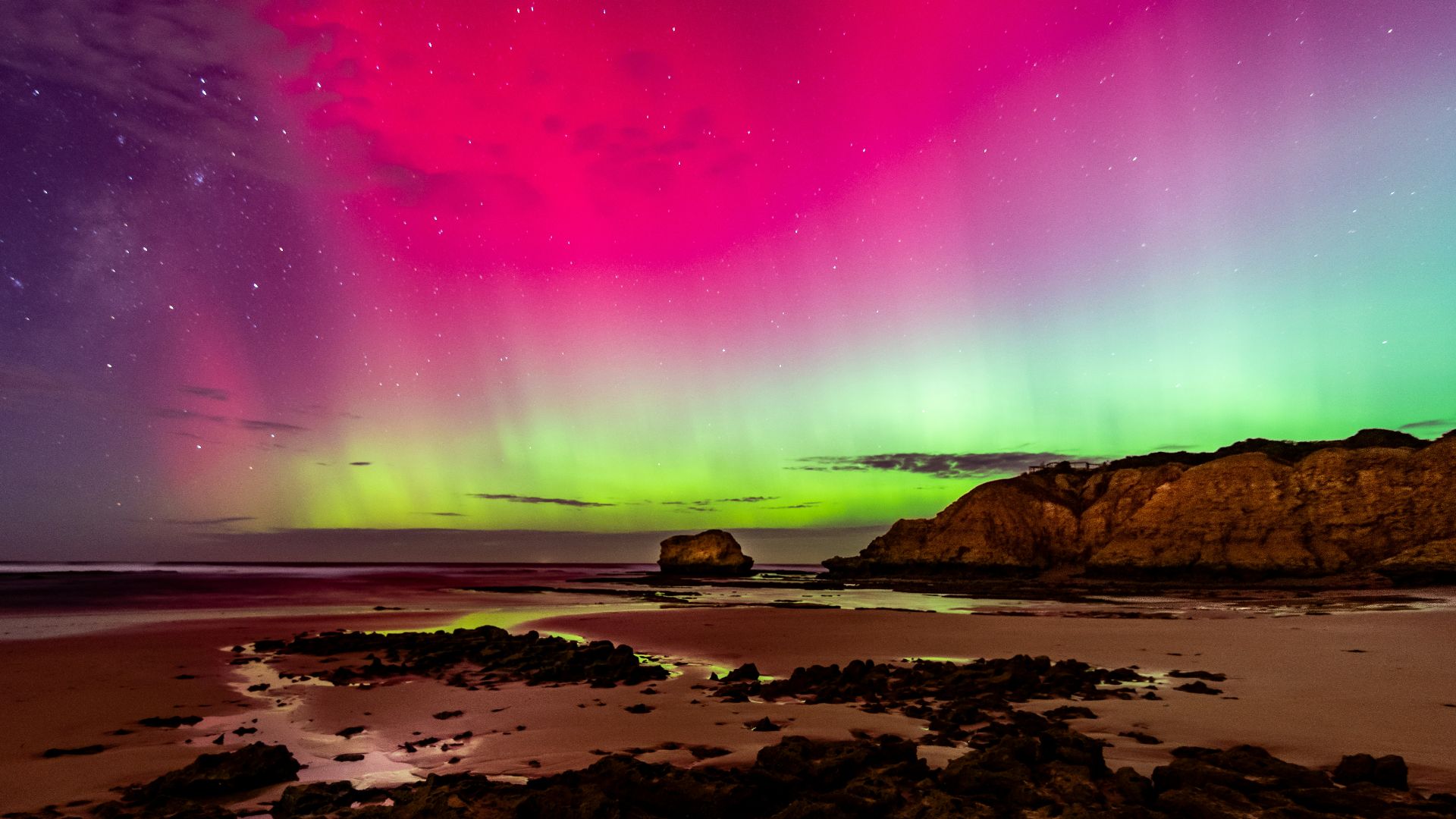 an aurora bore over a rocky beach under a purple sky