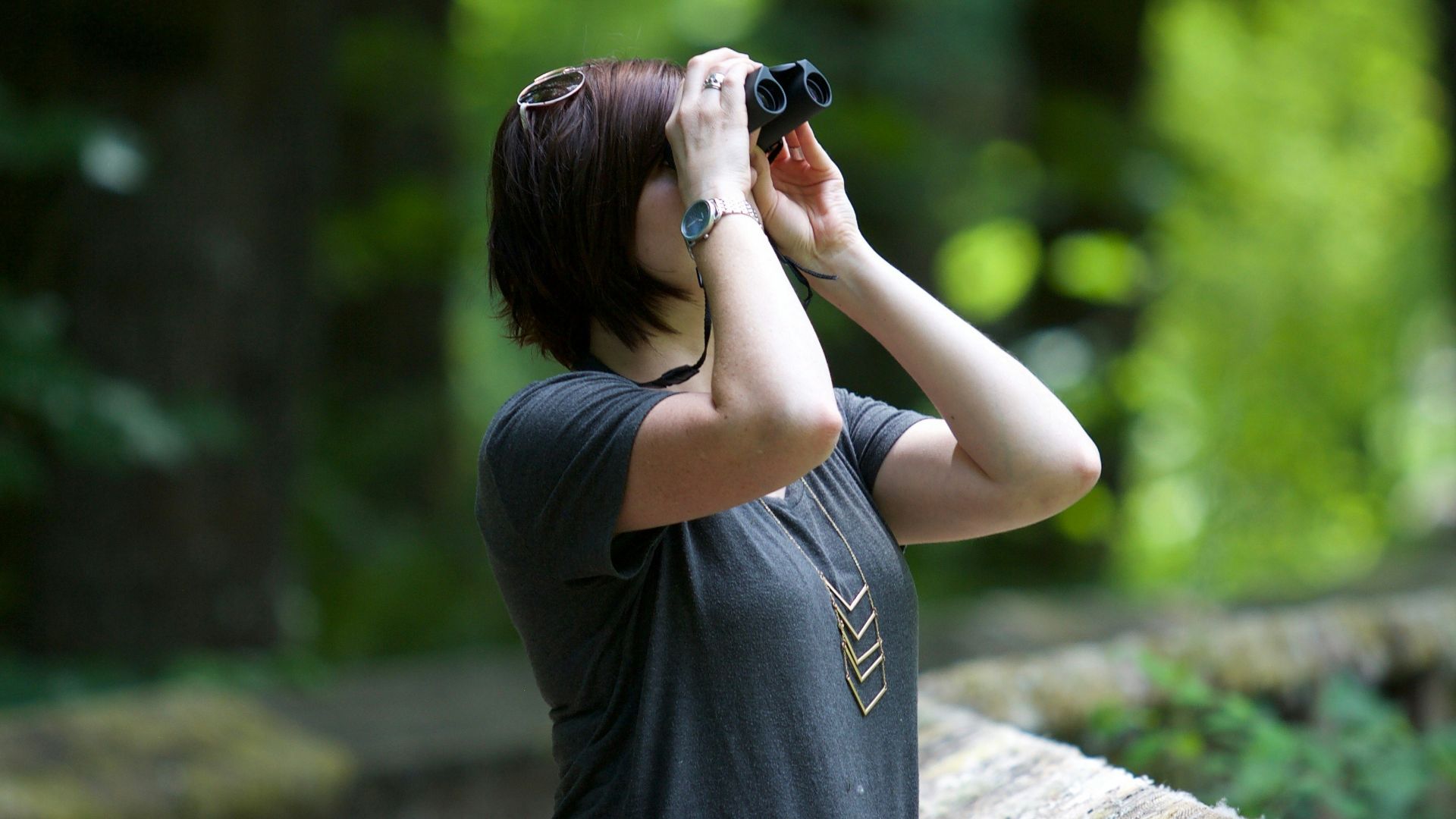 selective photography of woman holding binoculars looking upward outdoors