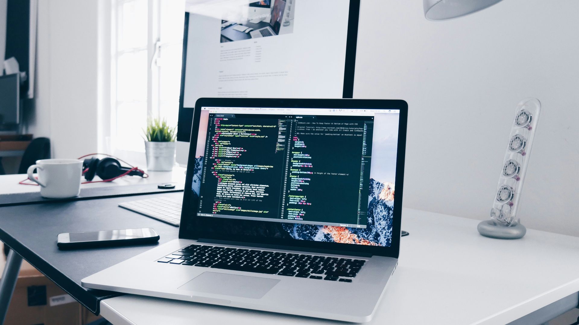 A MacBook with lines of code on its screen on a busy desk