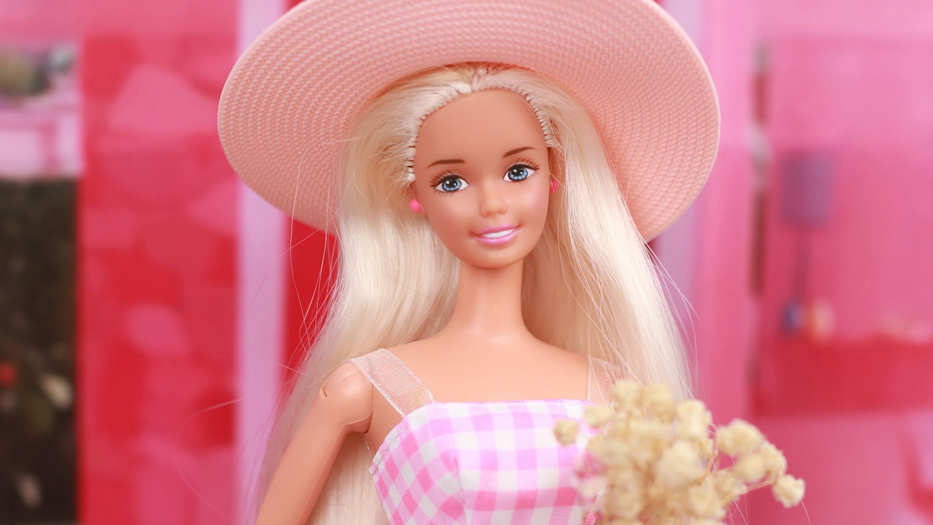 A barbie doll in a pink dress and hat on a pink motorcycle