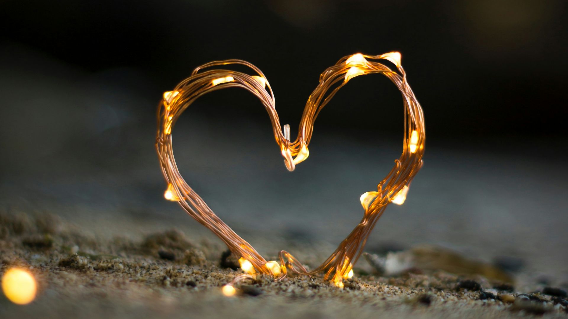 close-up photography of heart shaped fairy lite on brown sand
