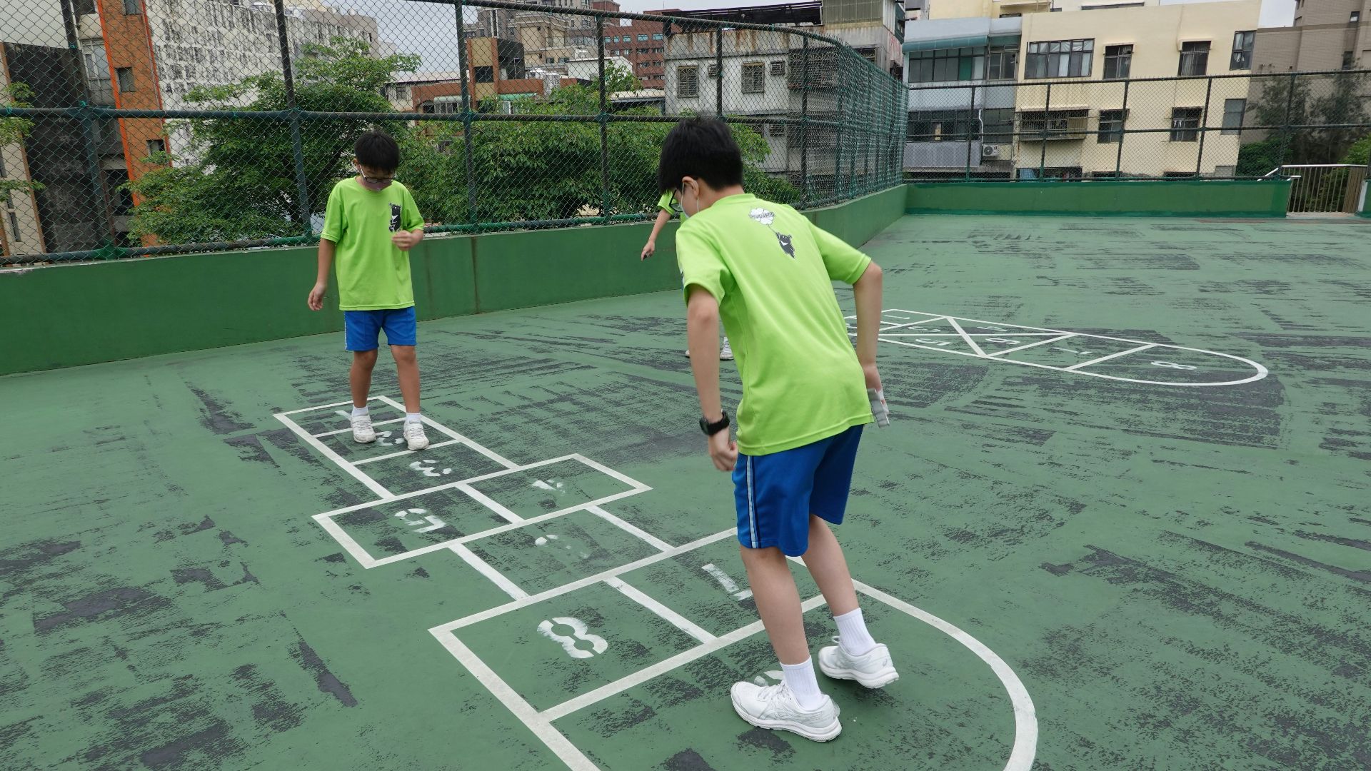 Two boys playing hopscotch on a rooftop court
