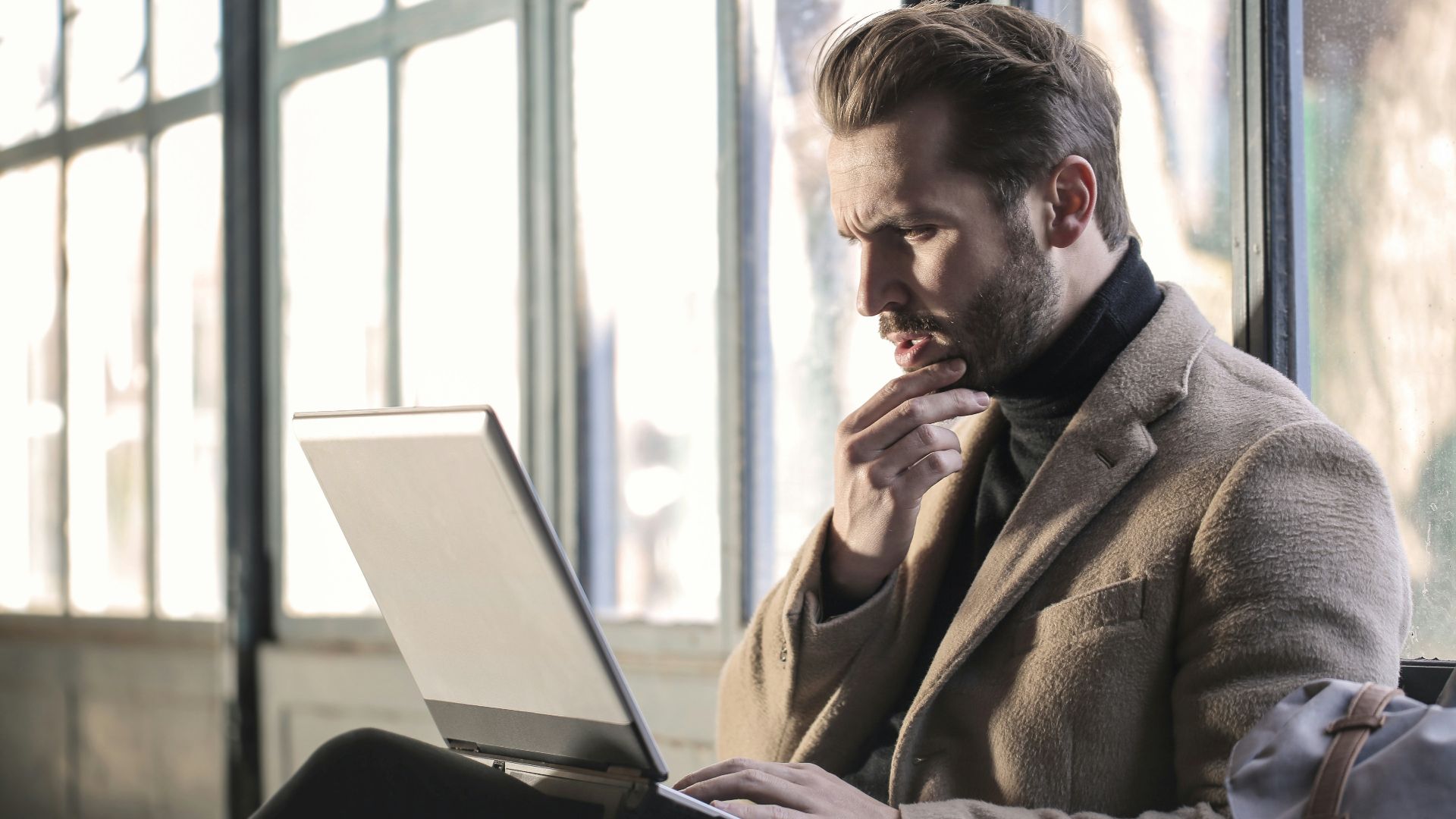 man holding his chin facing laptop computer