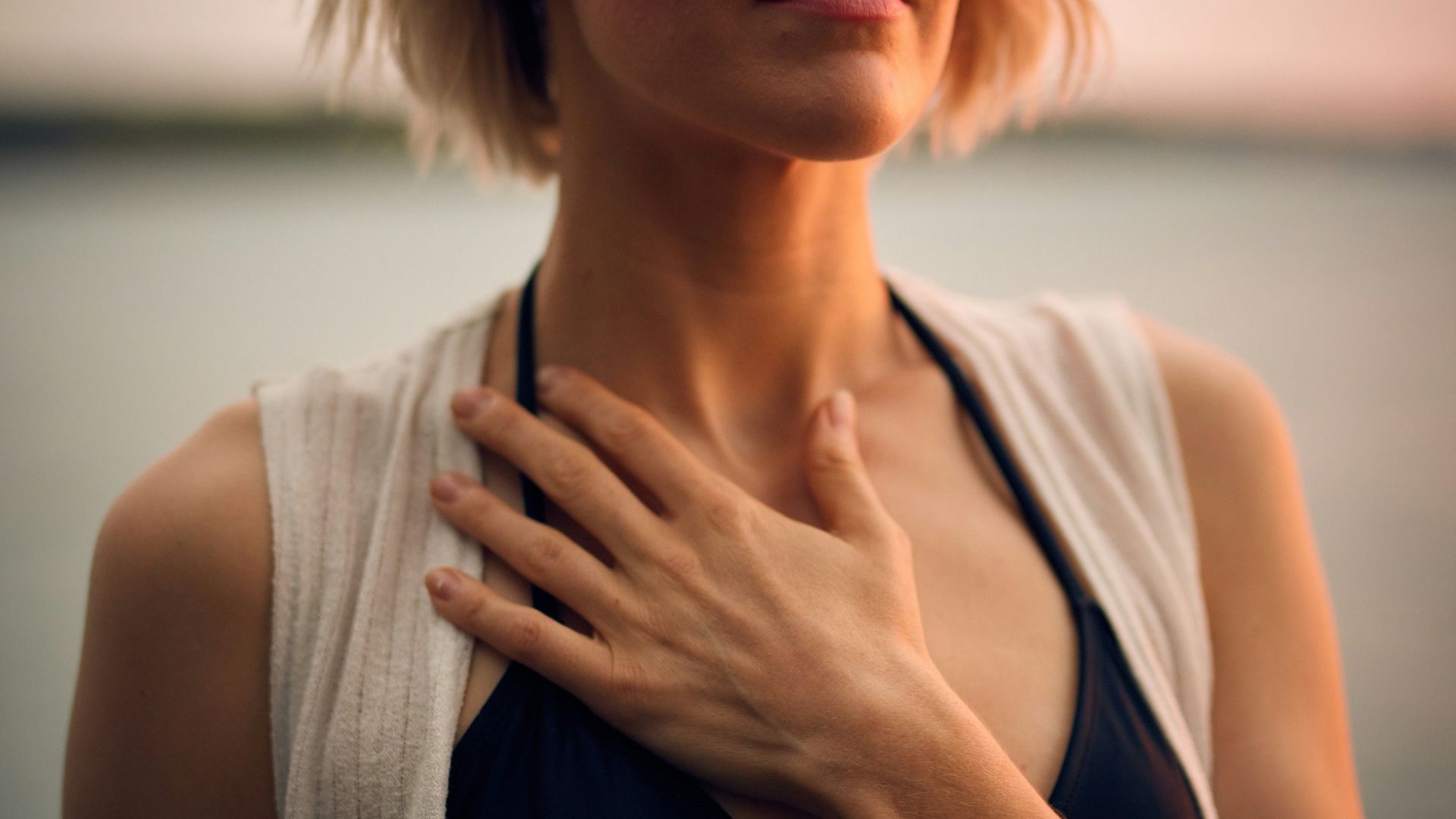 woman in white vest and black bikini with hand on chest