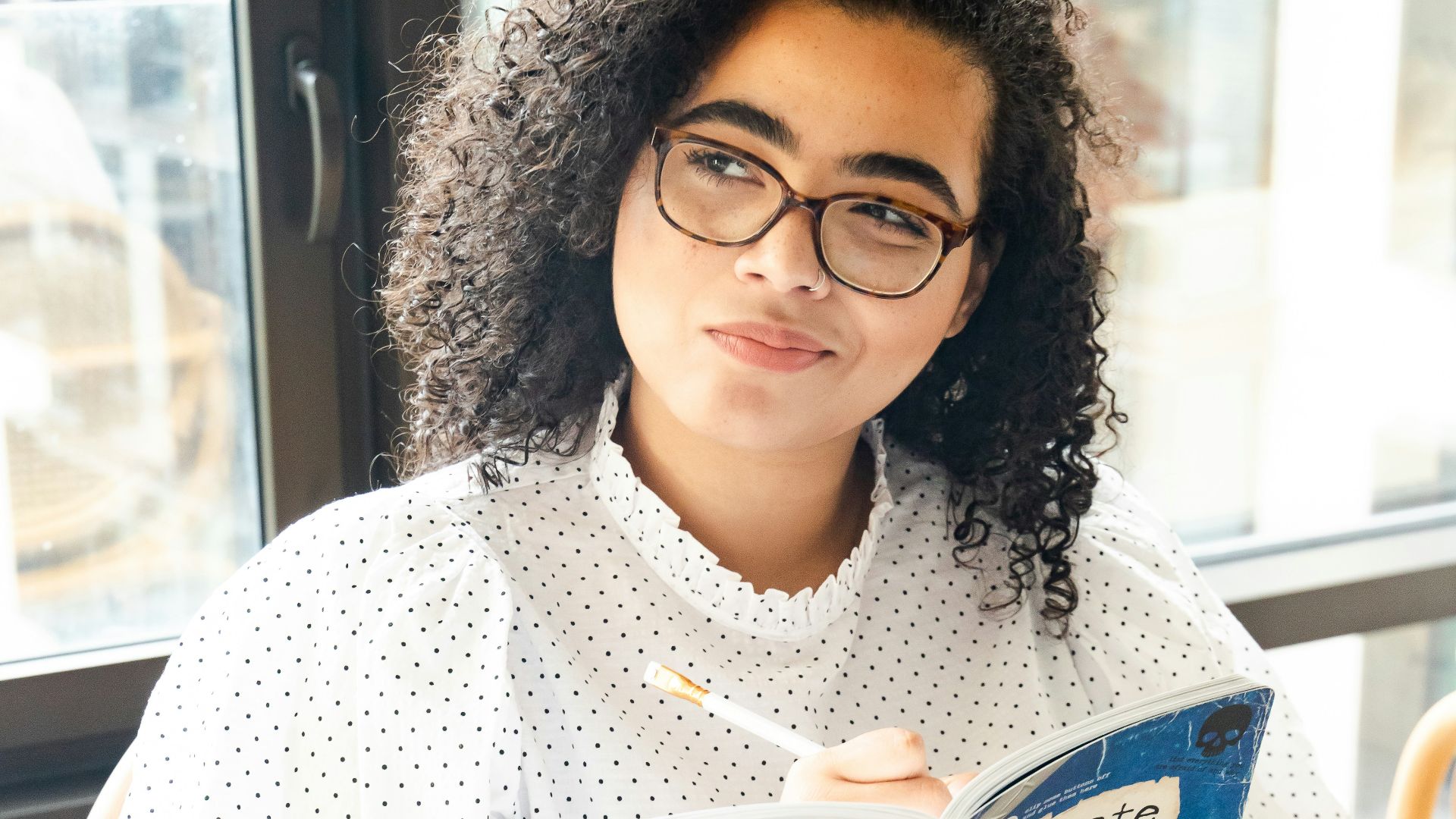 woman in white and black polka dot shirt holding blue and white book
