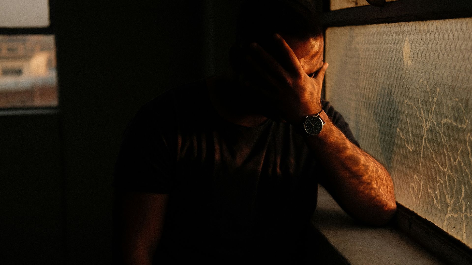 a man sitting in a window sill with his hand on his face