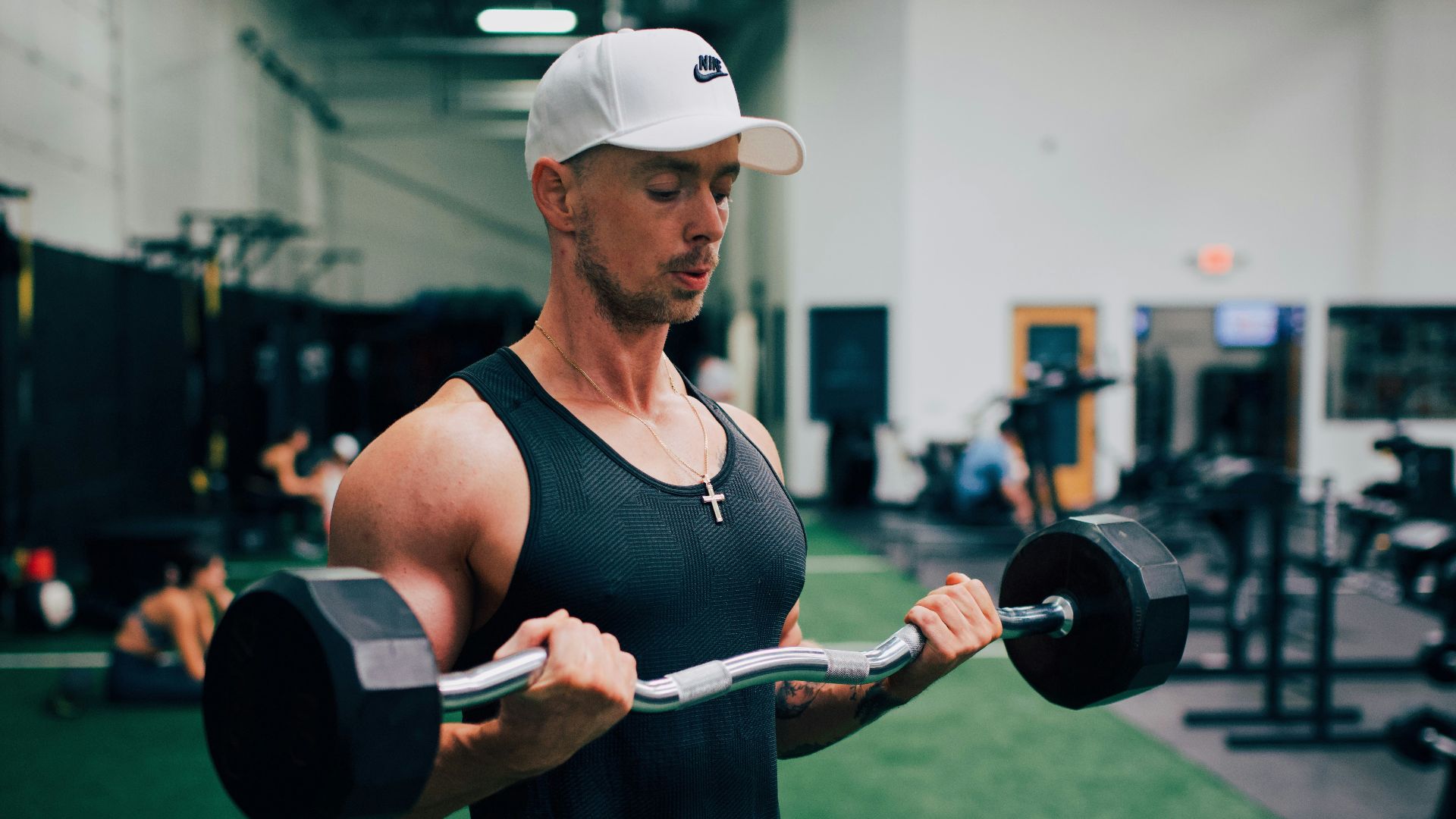 man in black tank top and white cap holding black and gray dumbbell