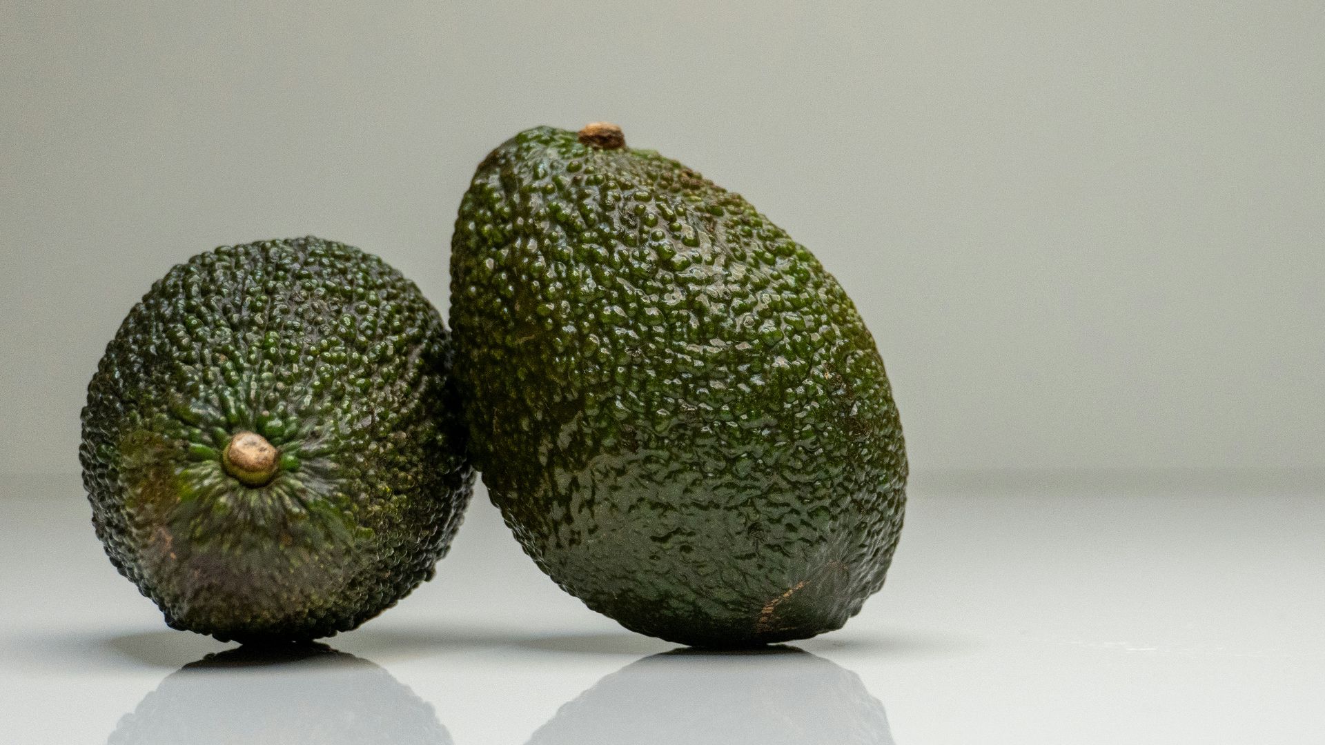 two avocados sitting side by side on a white surface