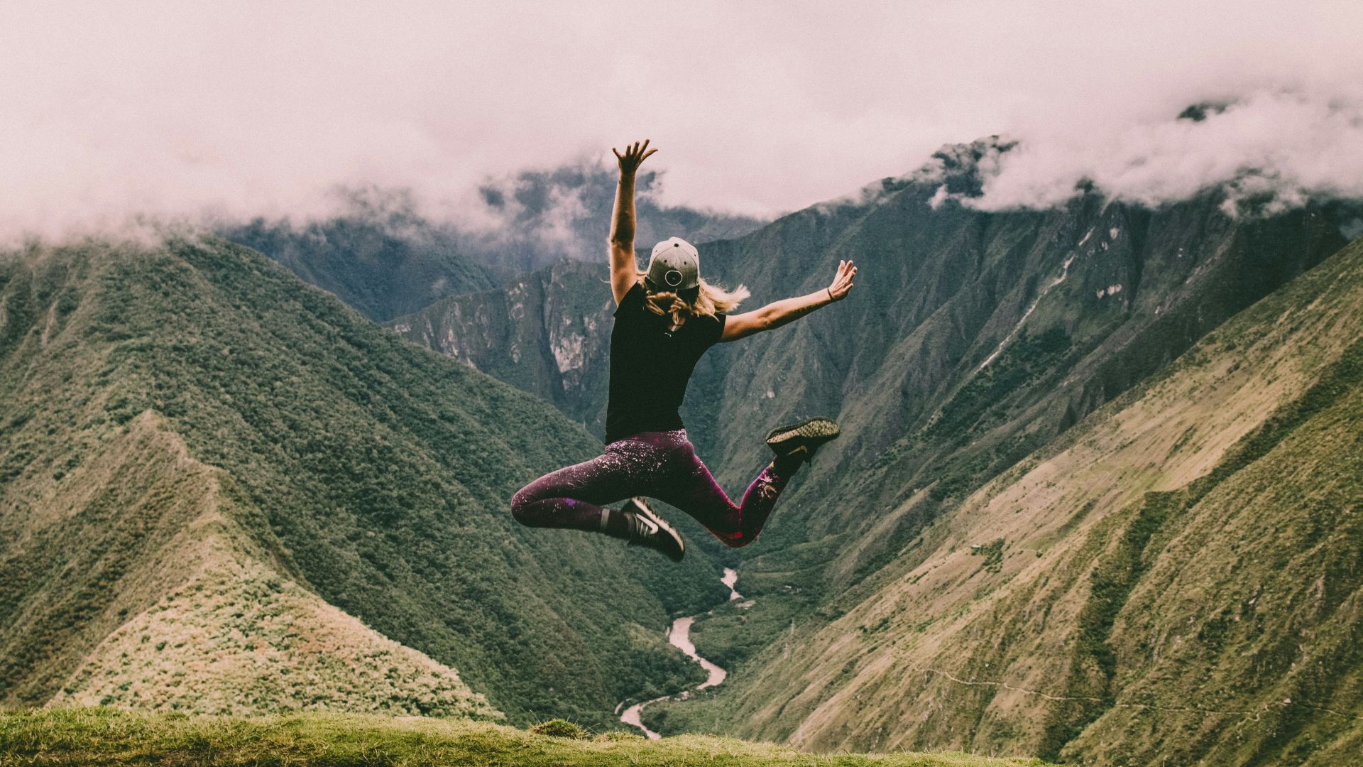 woman jumping on green mountains