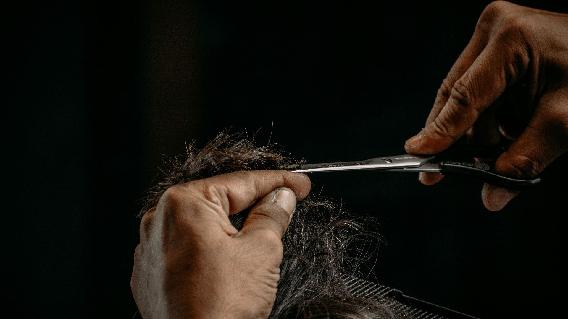 a person cutting a woman's hair with scissors