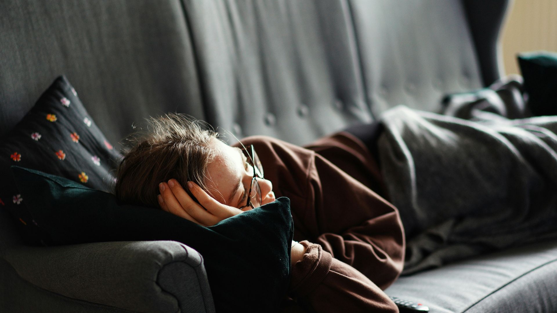 woman in pink jacket lying on gray couch