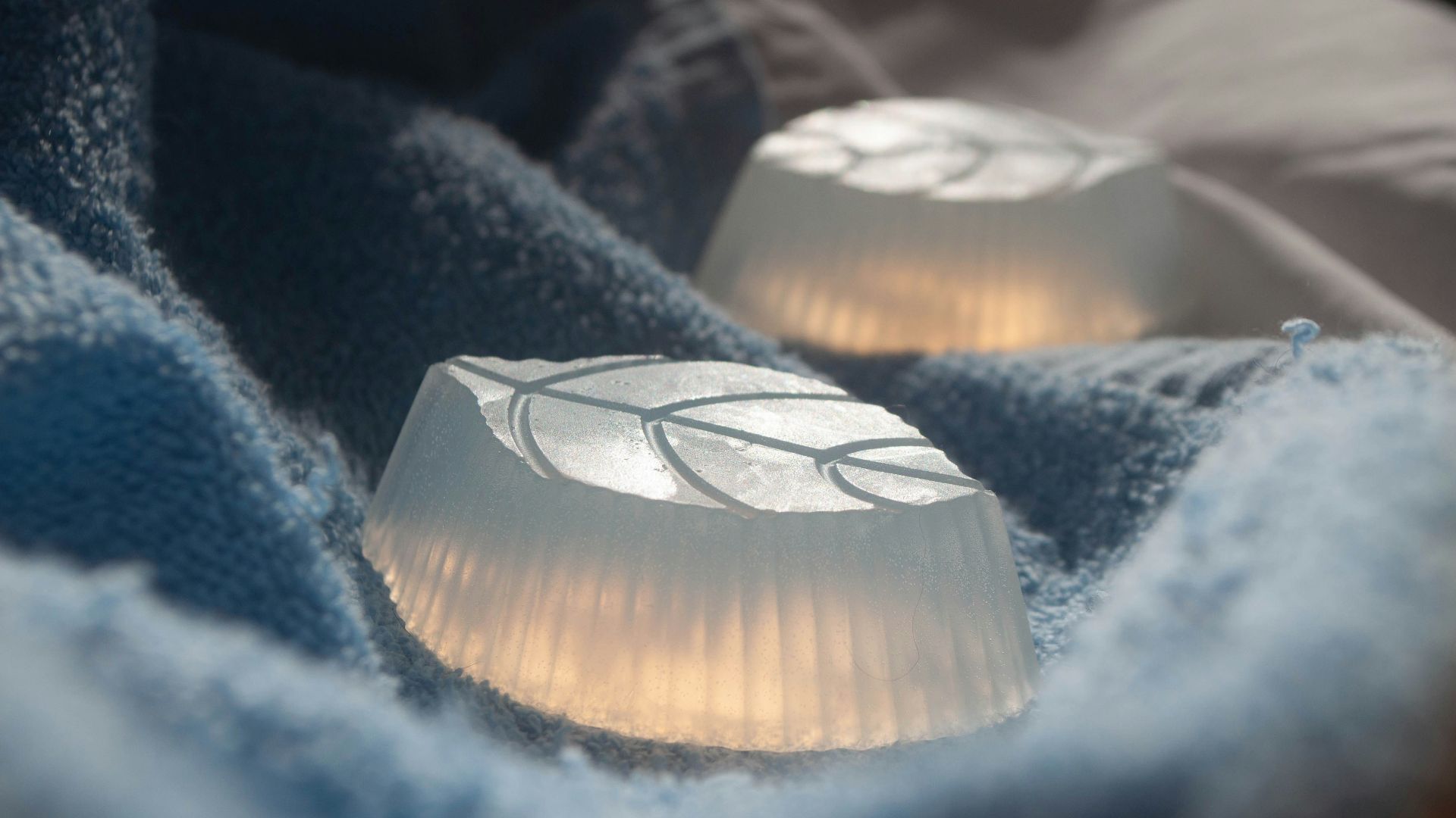 Two translucent soaps with leaf imprints resting on towels