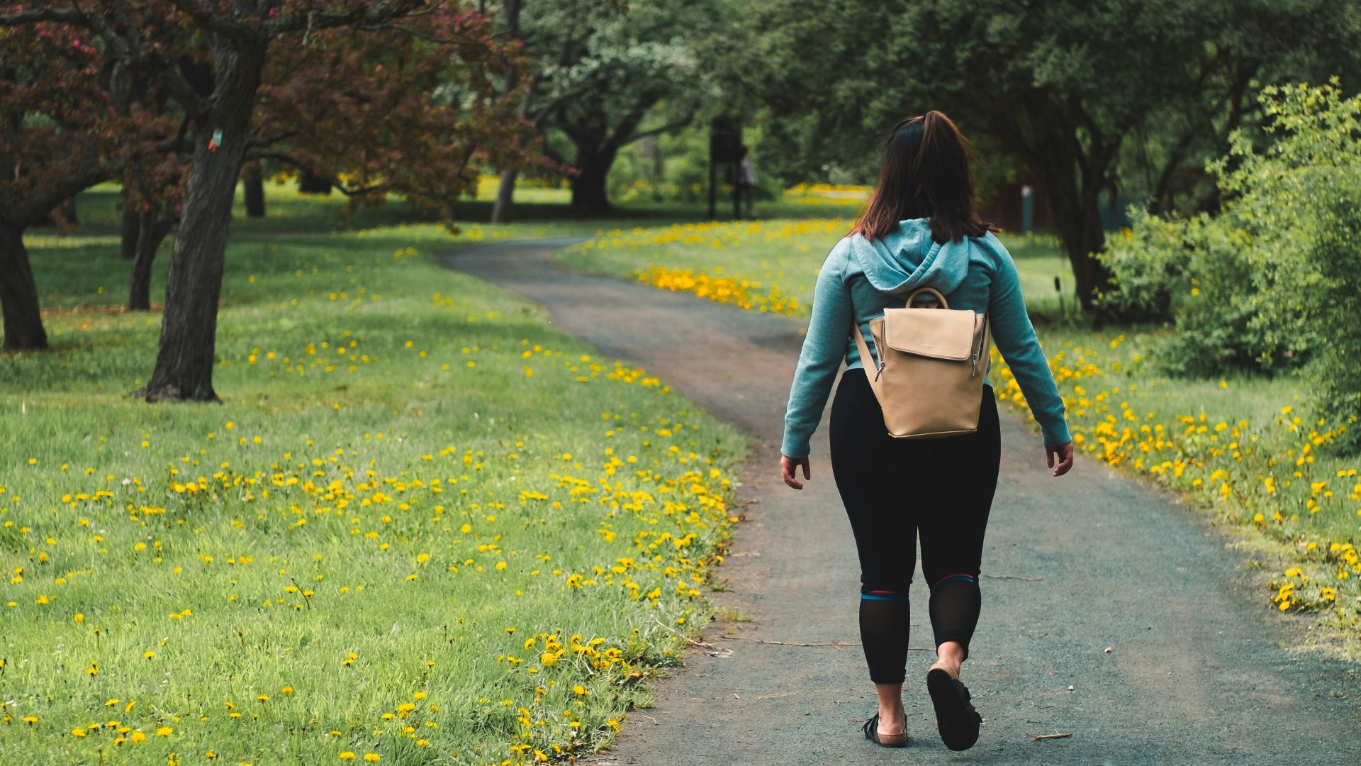 woman wearing blue jacket and black pants walking on grass field pathway
