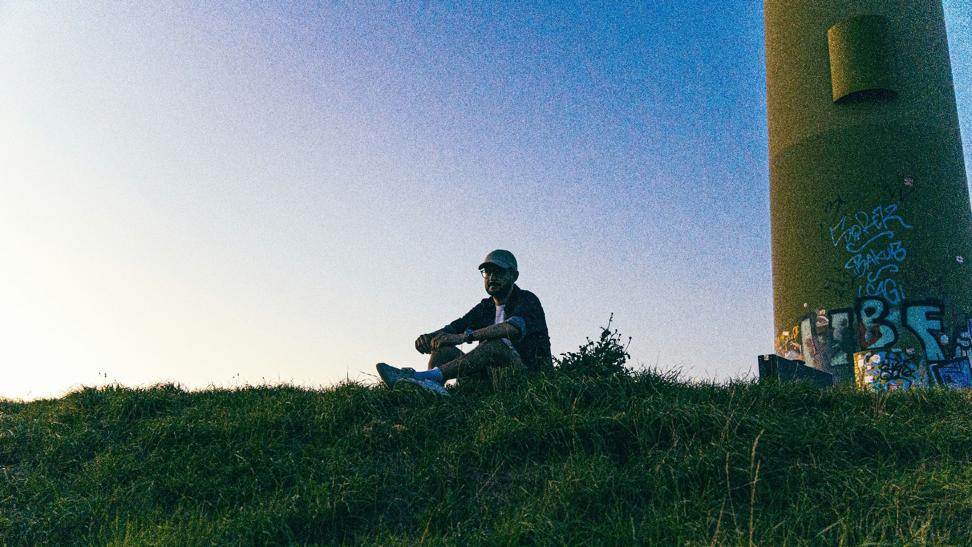 Man sitting on grassy hill near industrial structure