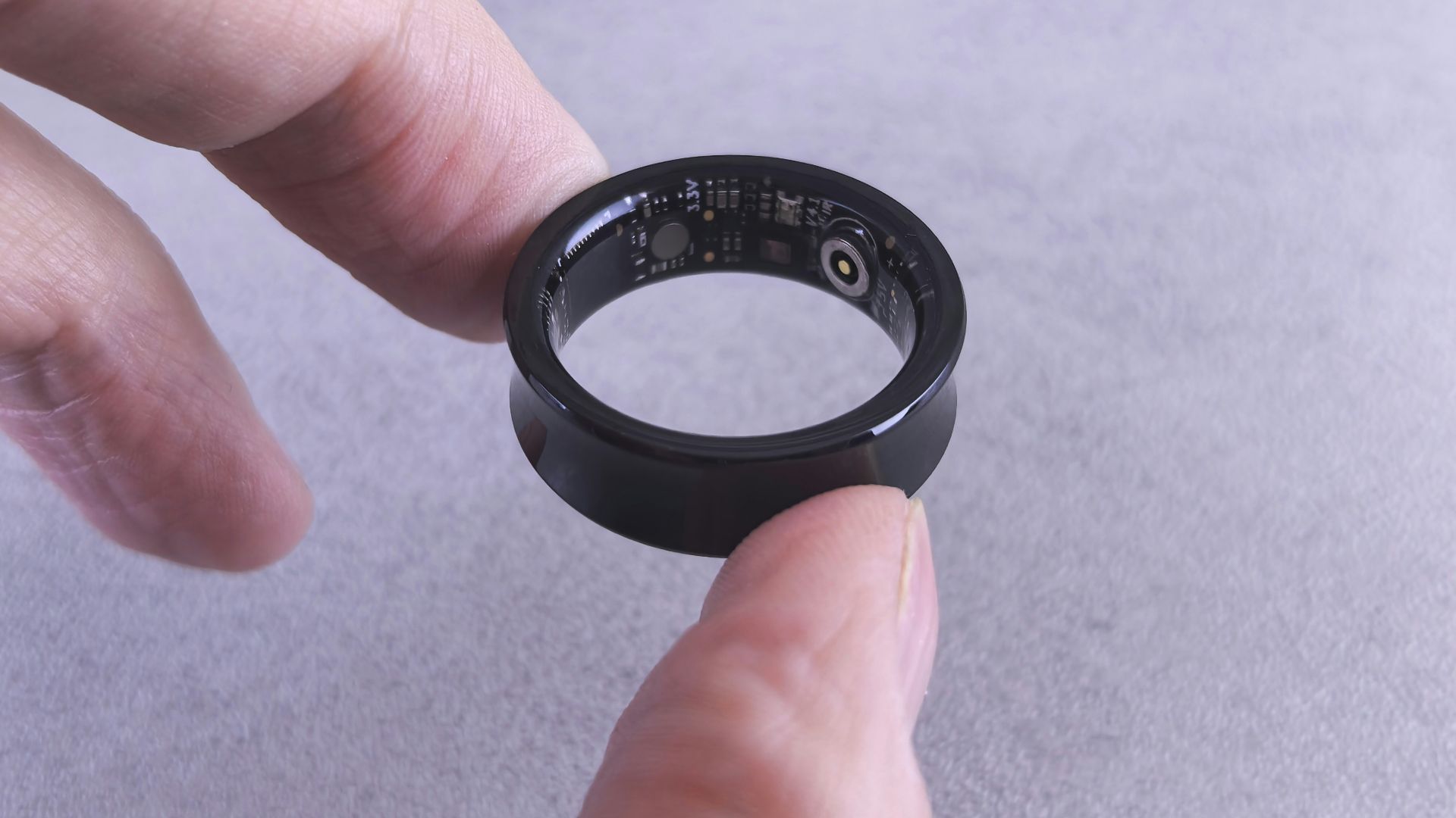 Fingers hold a black smart ring with circuits visible.