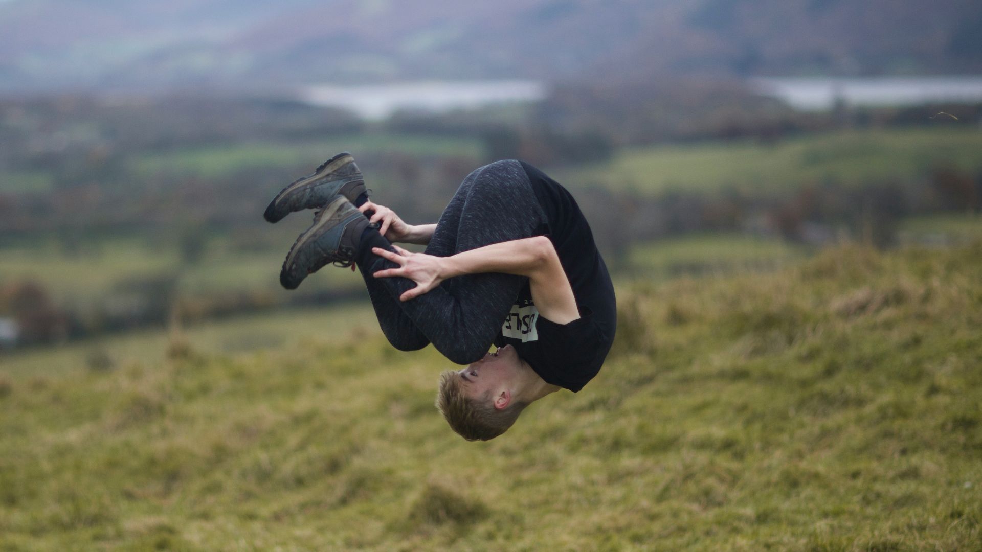 man wearing black crew-neck t-shirt tumbling on green field