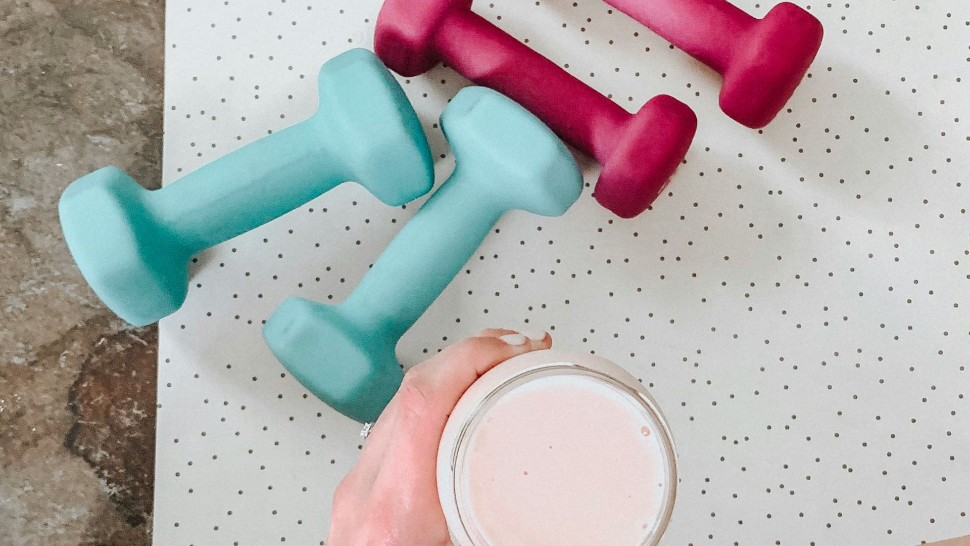person holding white liquid filled cup above two pairs of dumbbells