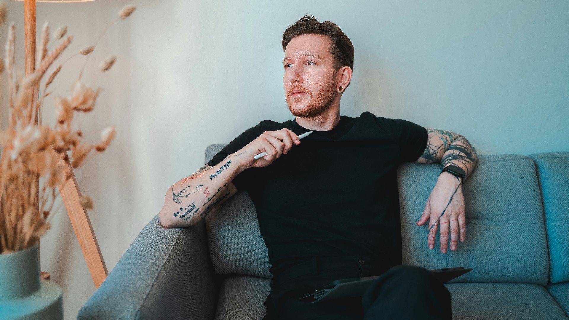 a man sitting on a couch with tattoos on his arm