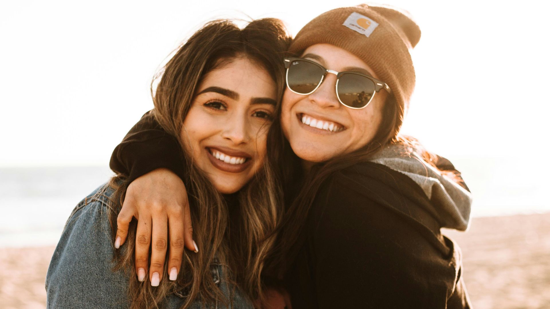 woman hugging other woman while smiling at beach