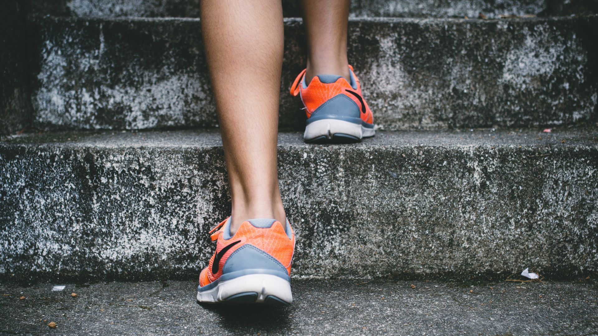 person wearing orange and gray Nike shoes walking on gray concrete stairs