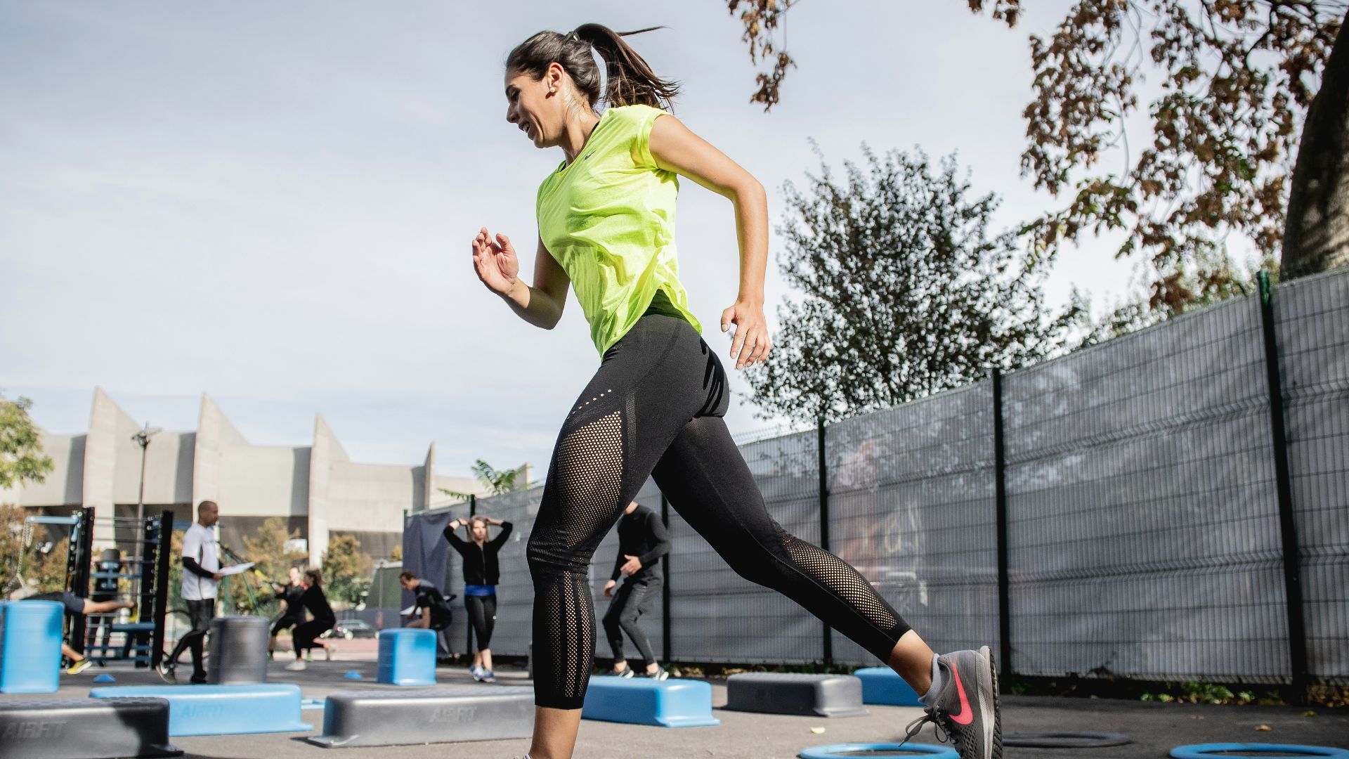 woman in green tank top and black leggings doing yoga on blue round trampoline