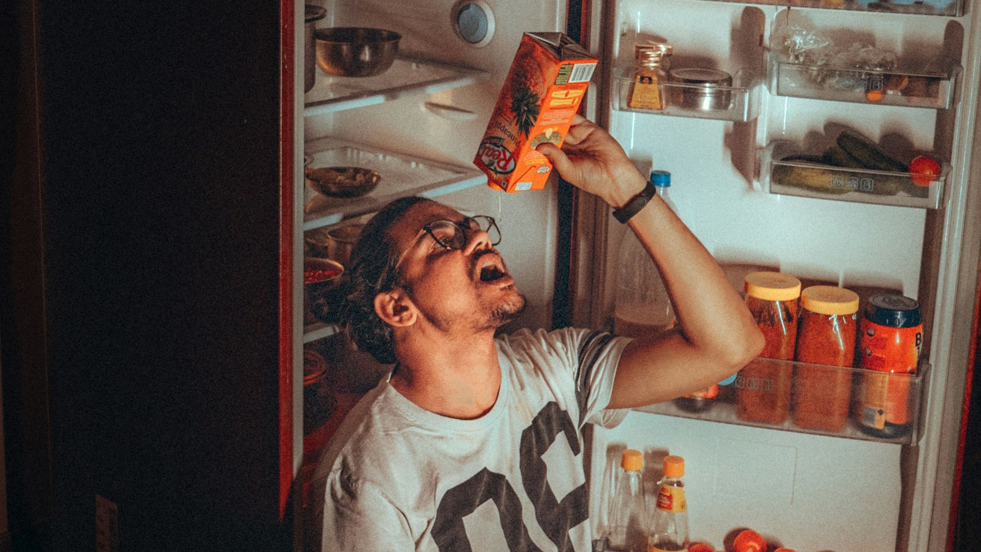 boy in white and black tank top standing beside red top mount refrigerator