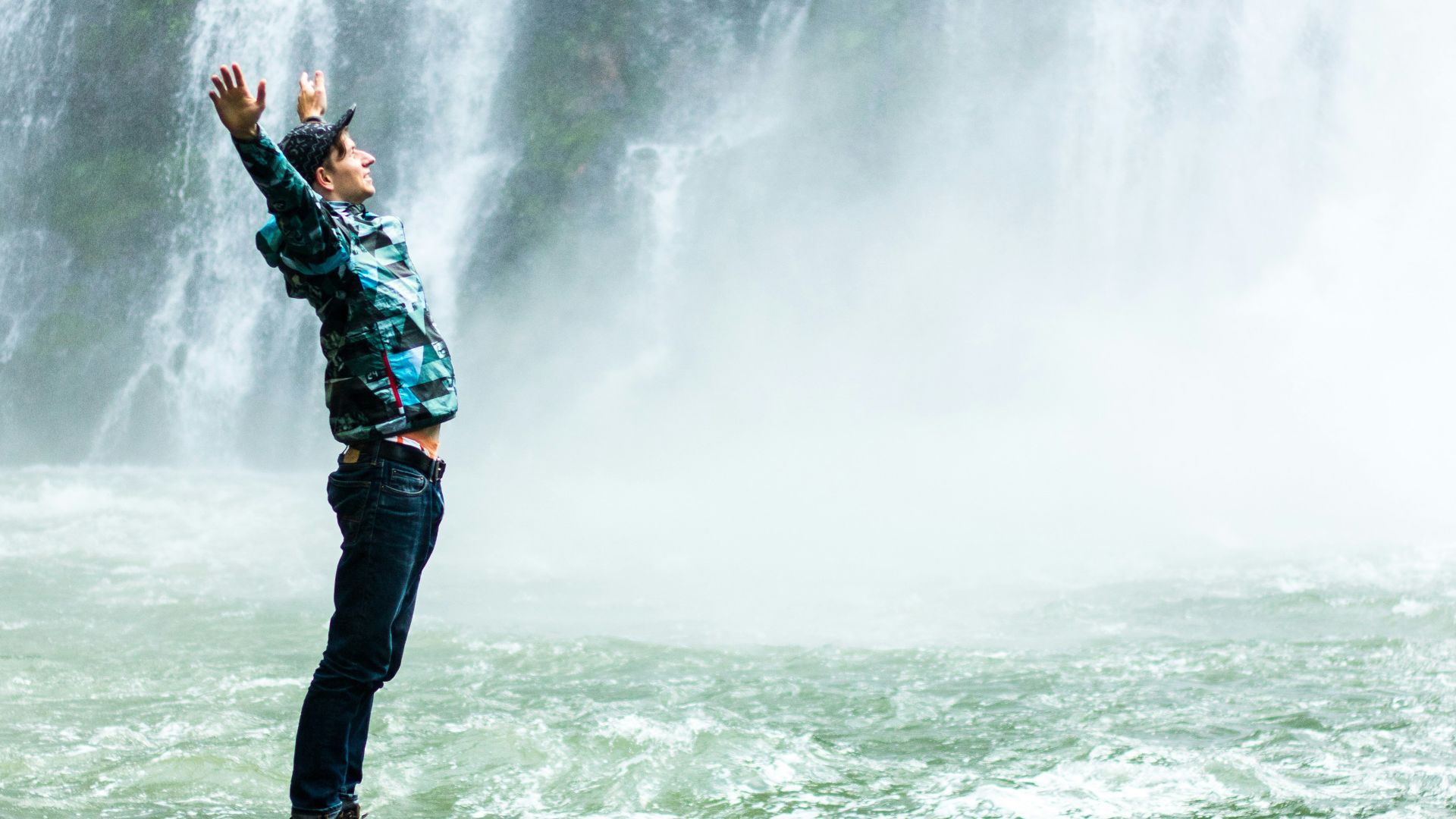 man standing on black rock surrounded body of water