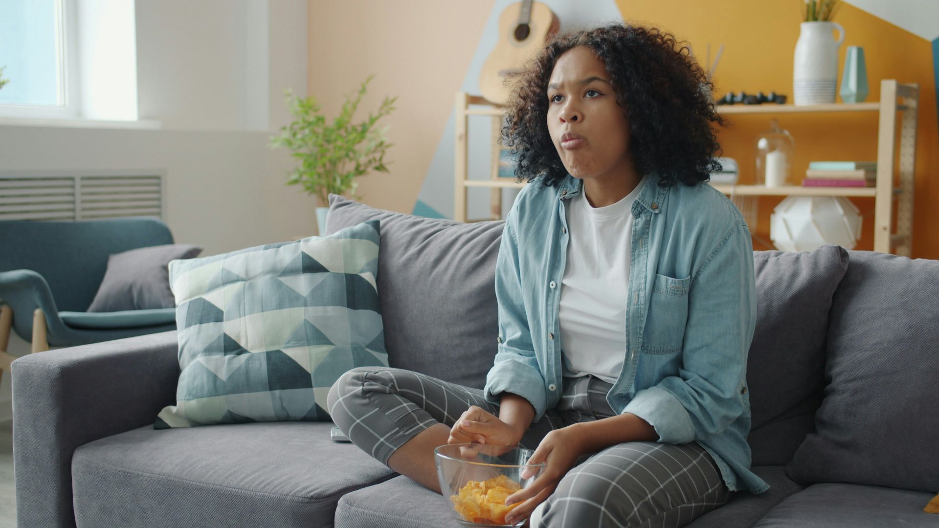 A woman eating chips while watching television on the couch.