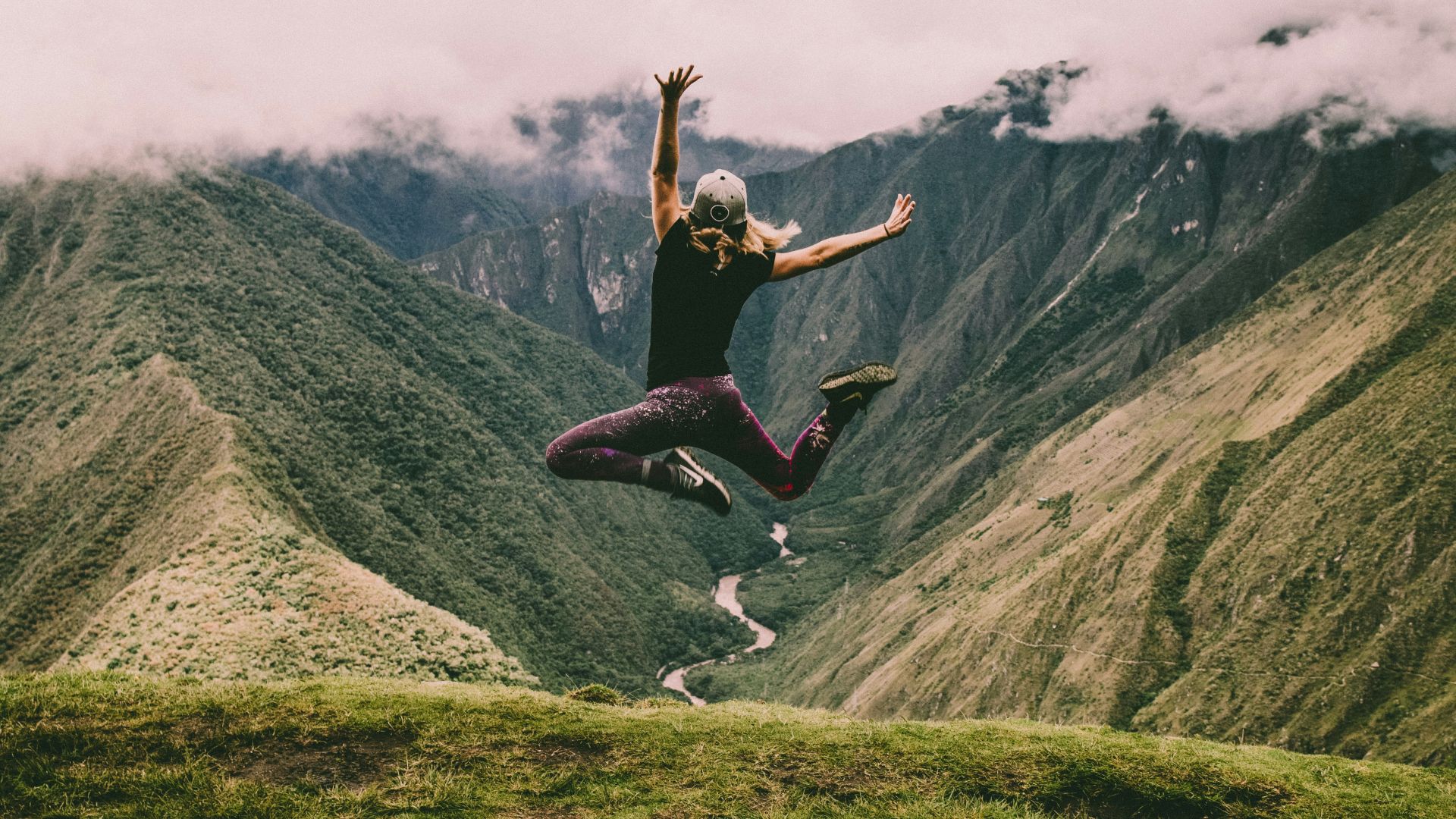 woman jumping on green mountains