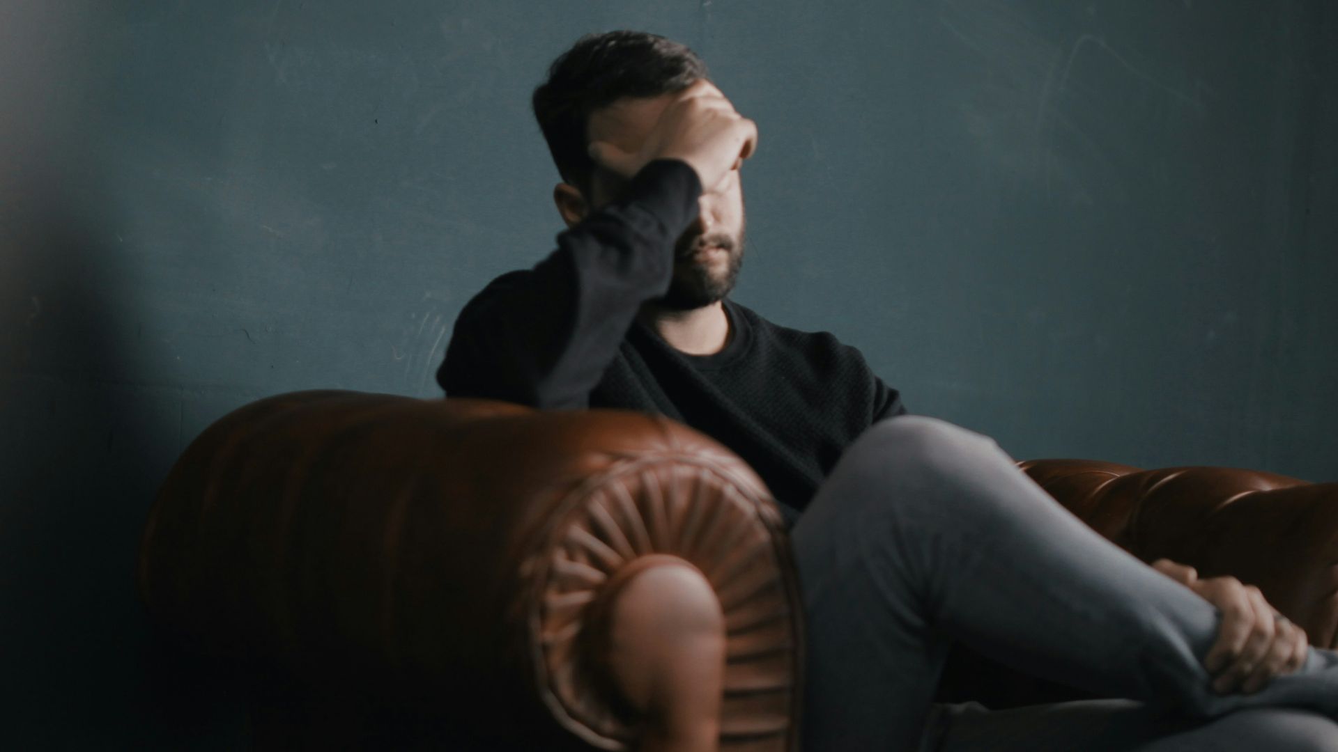 a man holds his head while sitting on a sofa
