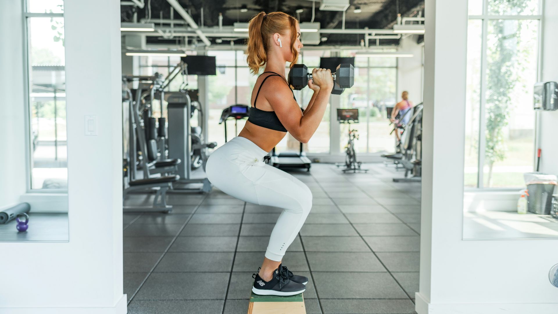 woman wearing black sports bra and white legging lifting dummbells
