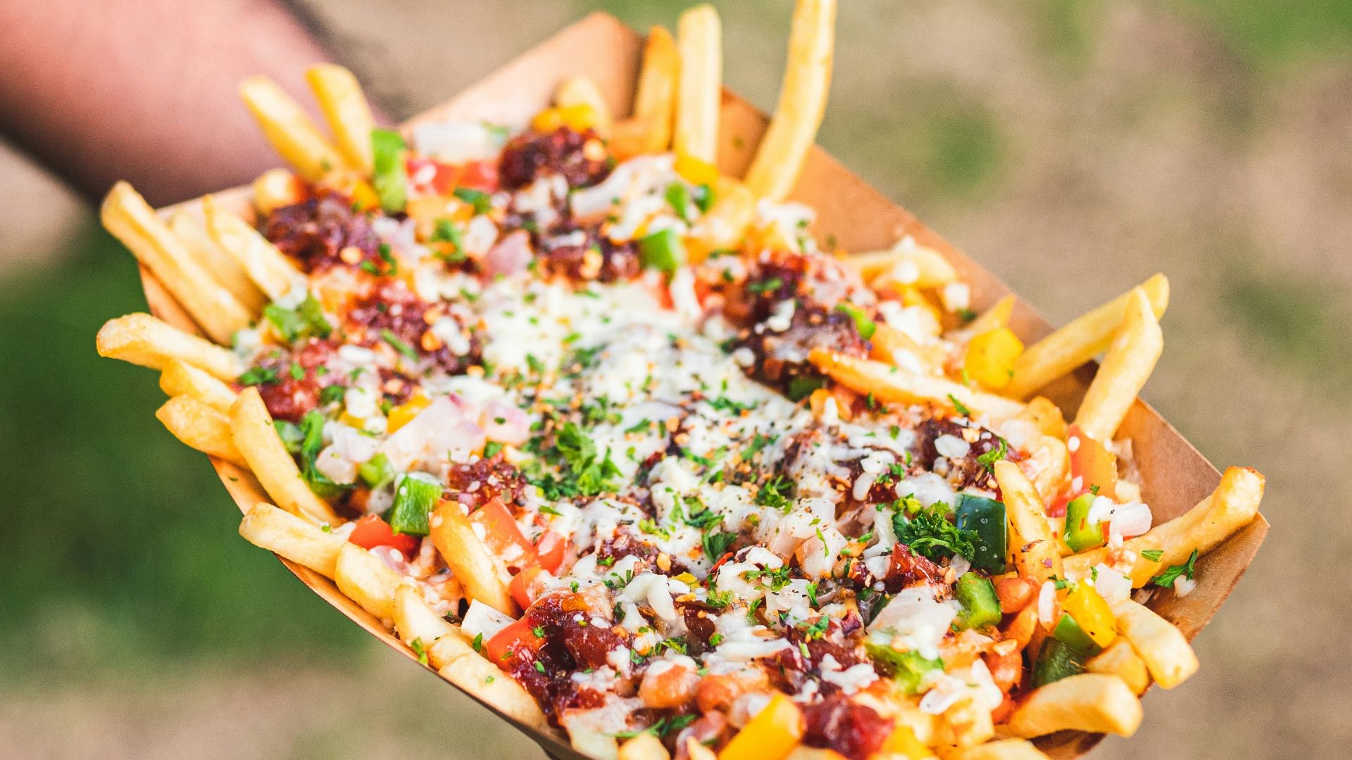 a person holding a tray of fries with cheese and other toppings