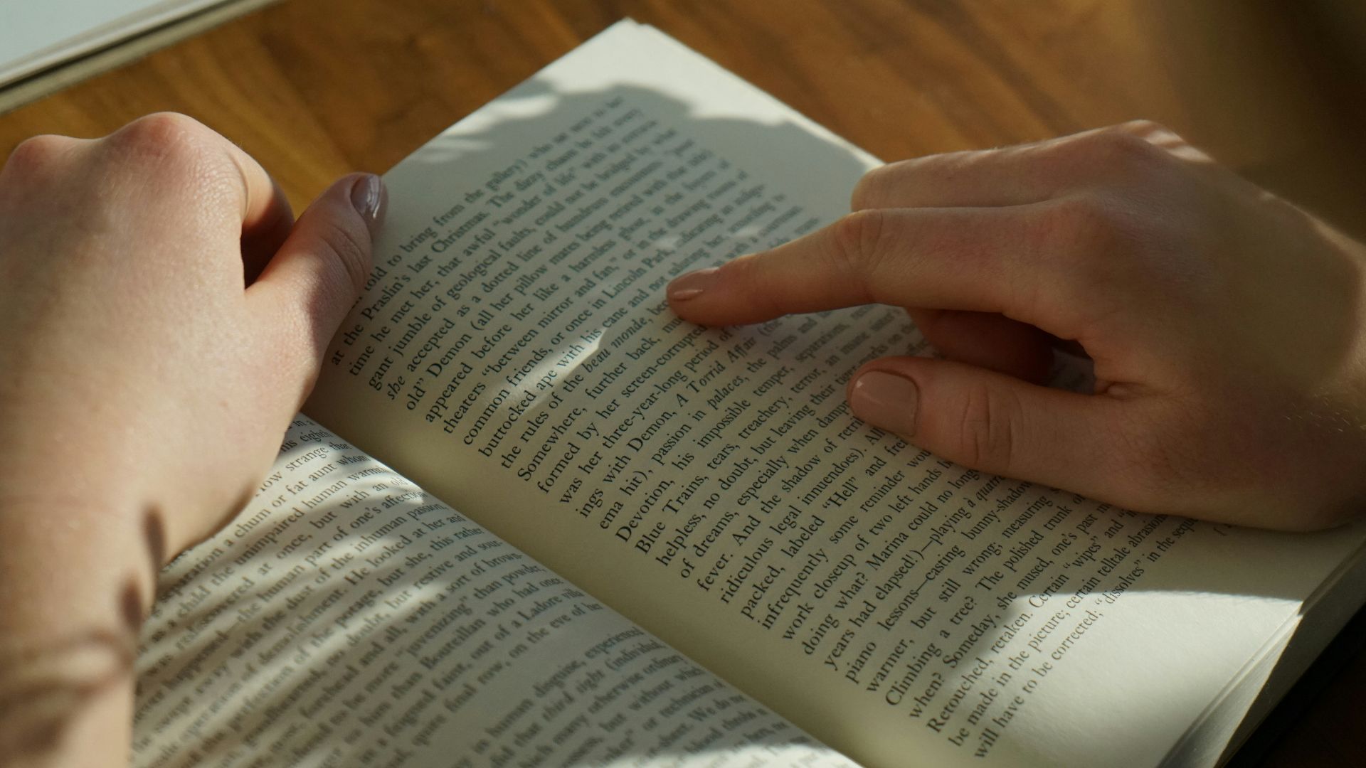 person reading book on brown wooden table taken at daytome