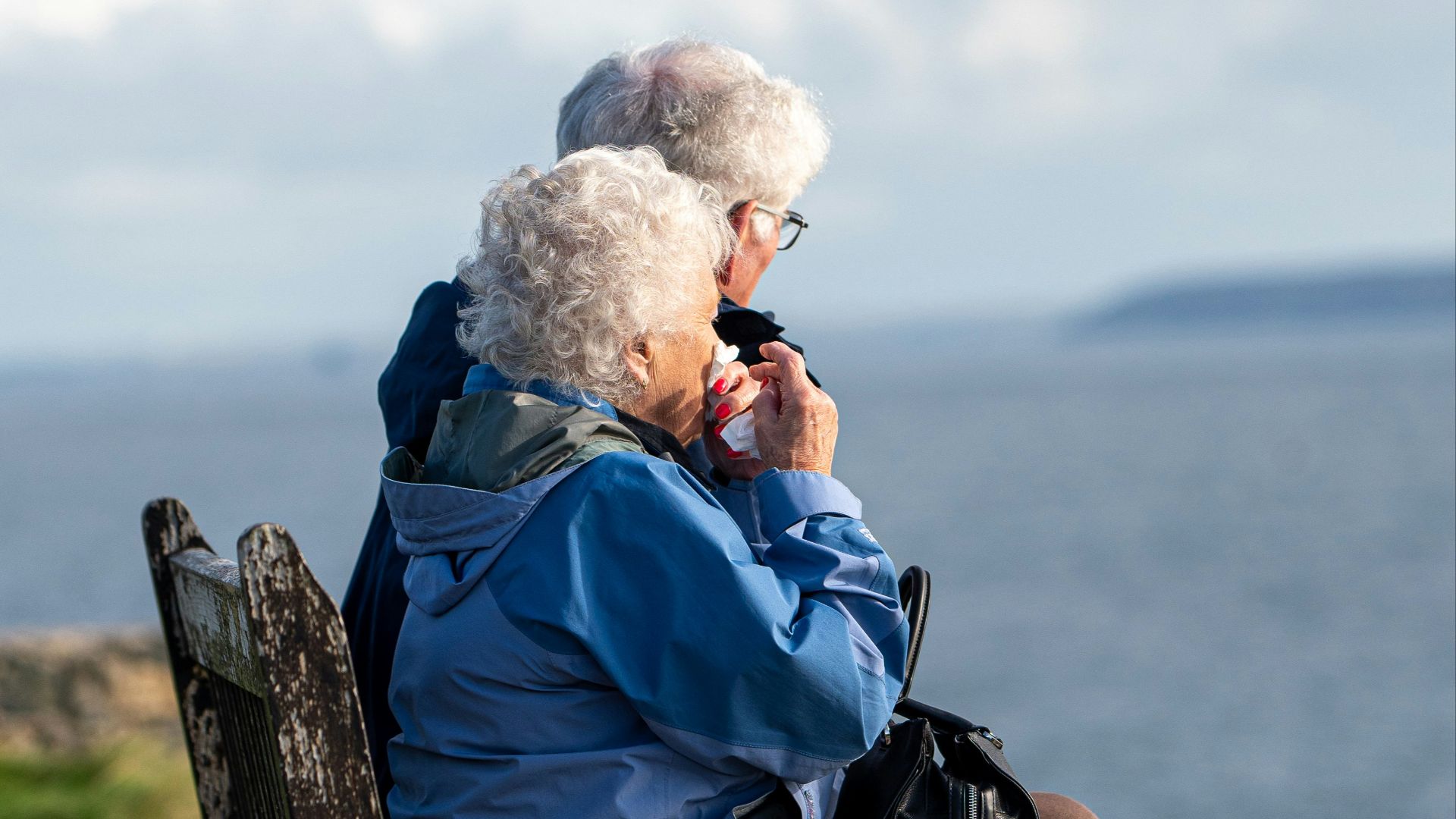 man and woman sitting on gray wooden bench viewing blue sea during daytime