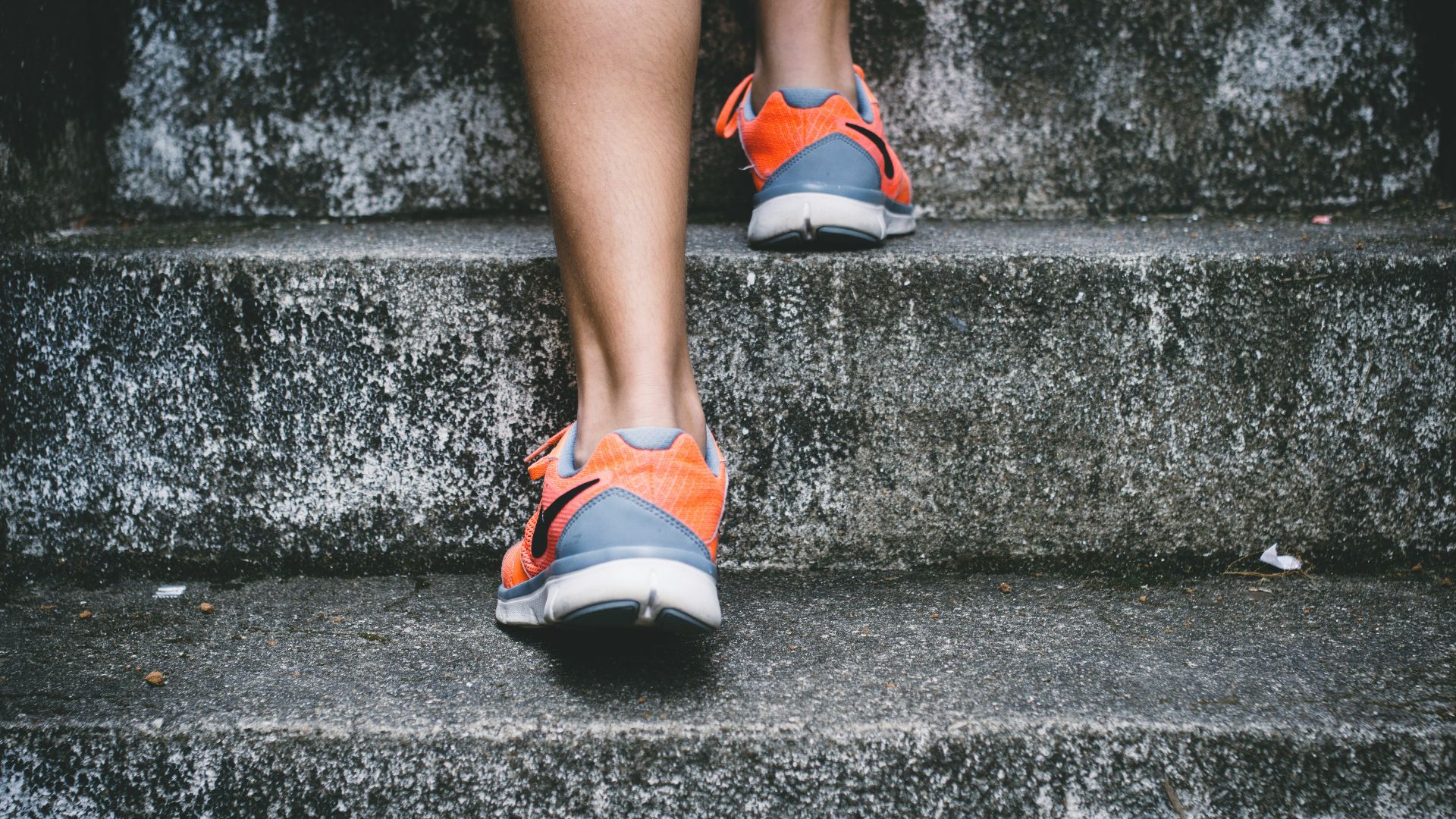 person wearing orange and gray Nike shoes walking on gray concrete stairs