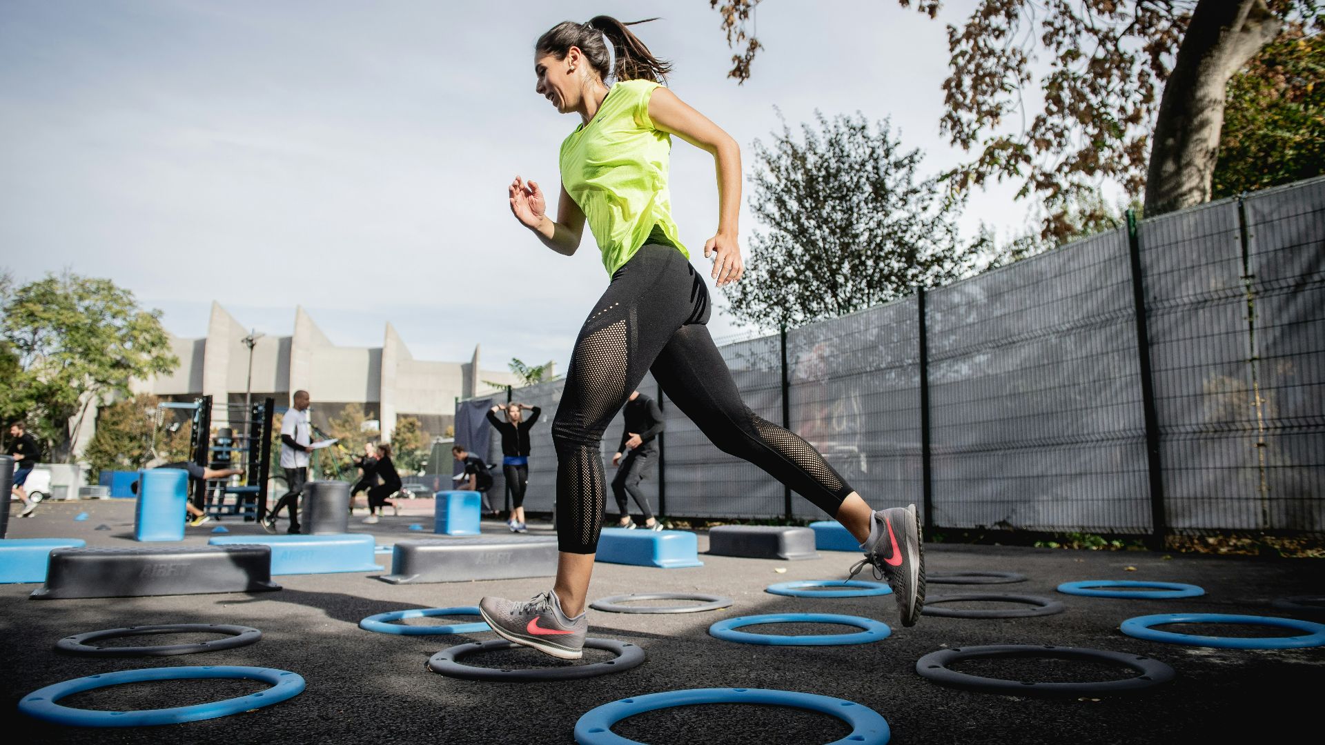 woman in green tank top and black leggings doing yoga on blue round trampoline