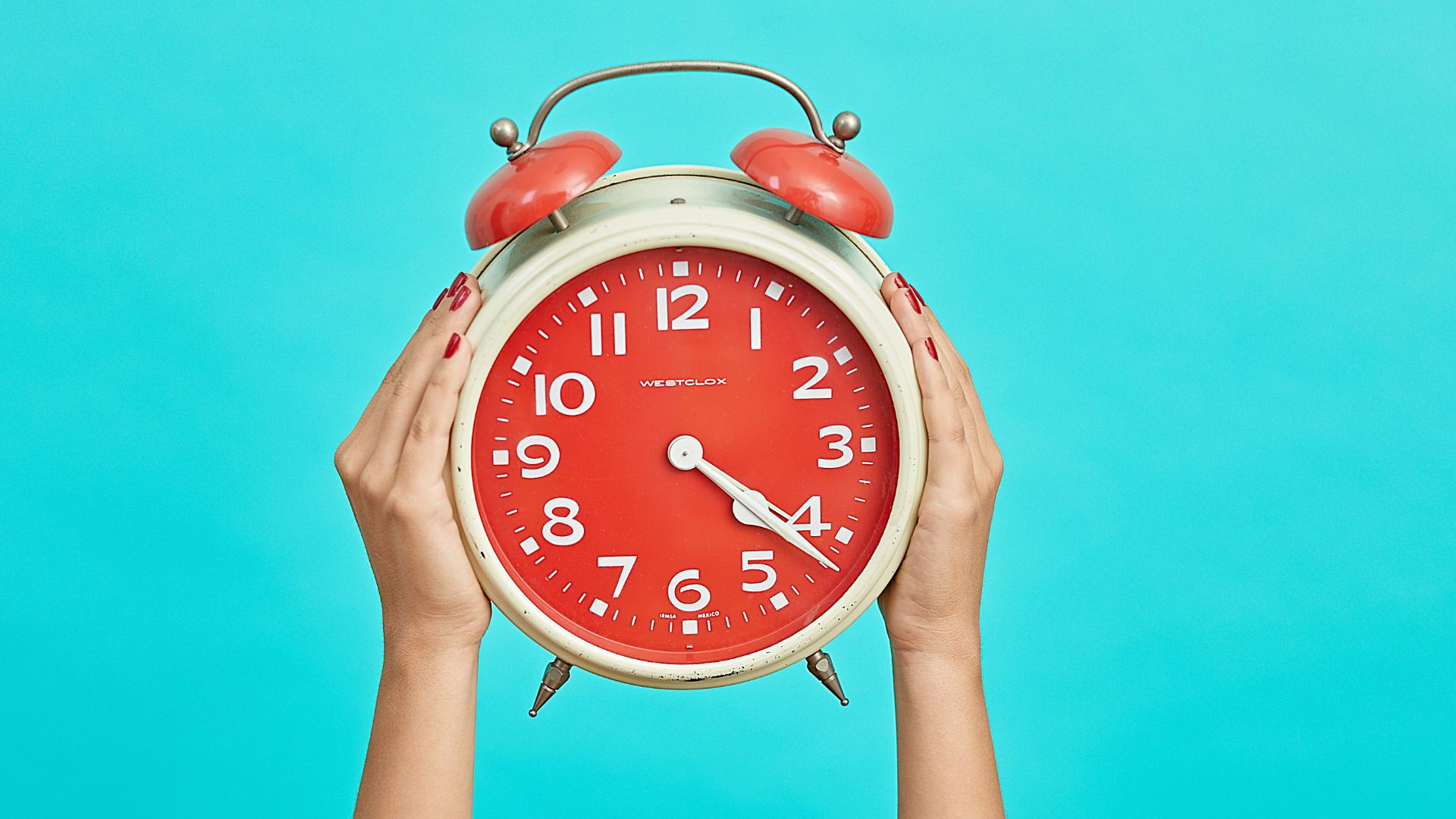 person holding red and beige twin bell analog alarm clock