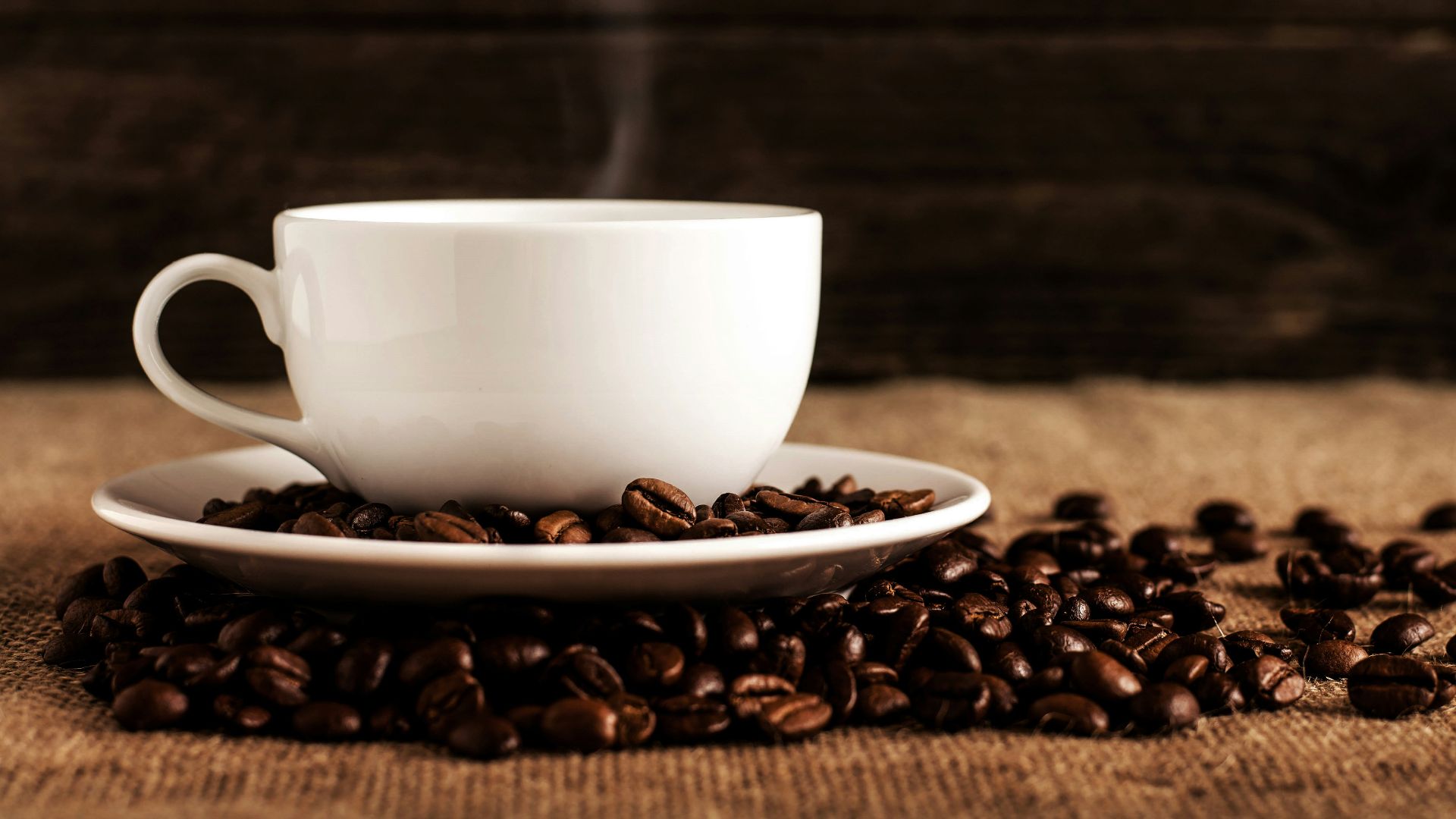 white ceramic mug and saucer with coffee beans on brown textile