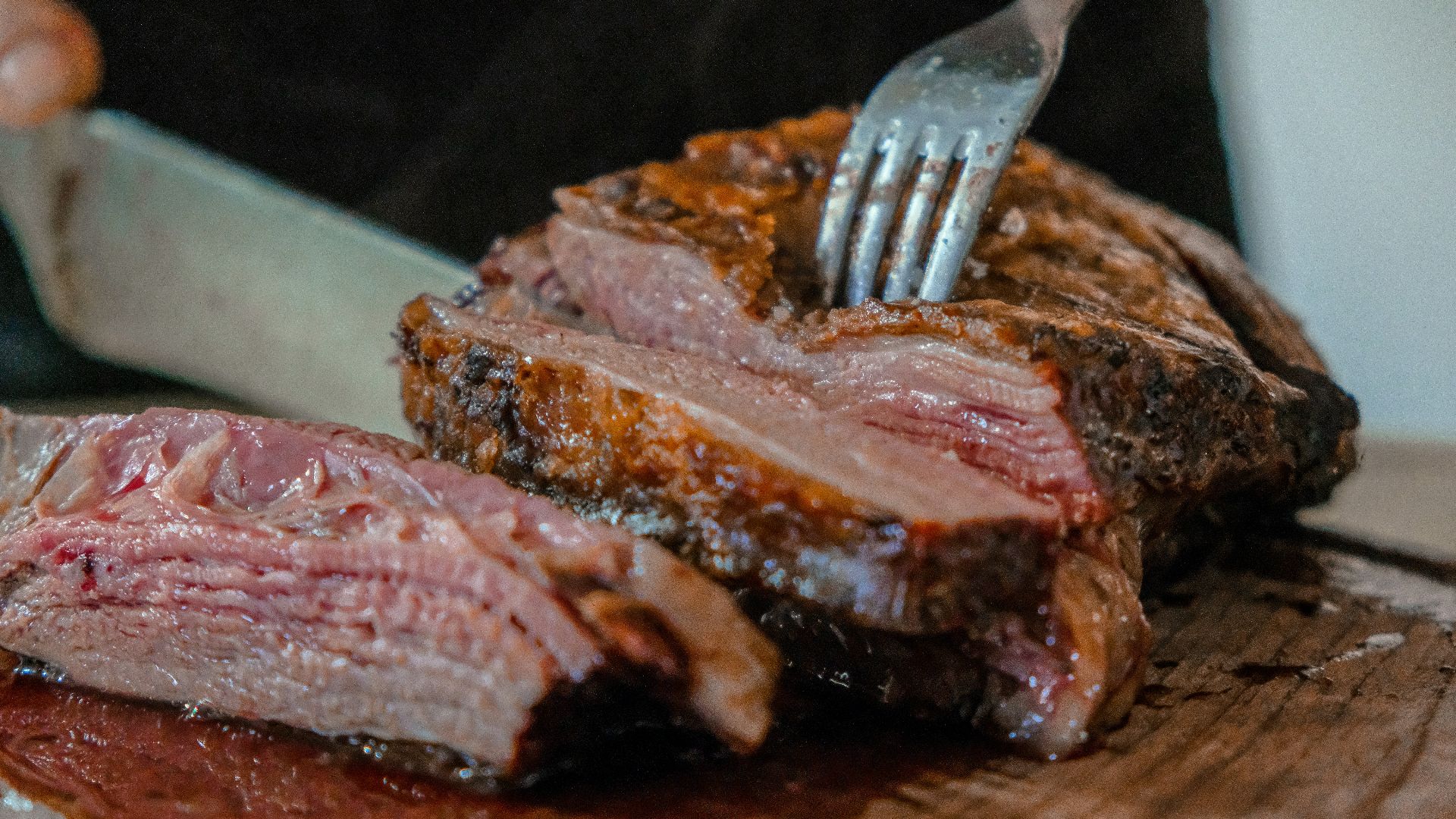 person slicing a meat on brown wooden board
