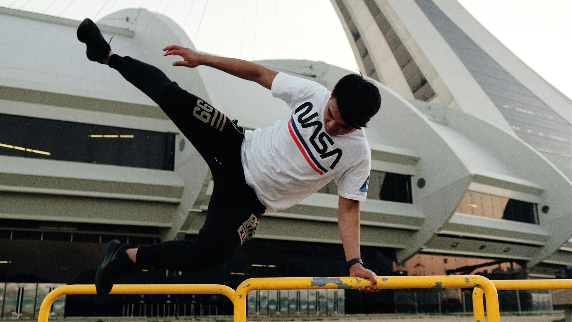 man in white and red long sleeve shirt and black pants jumping on yellow metal bar