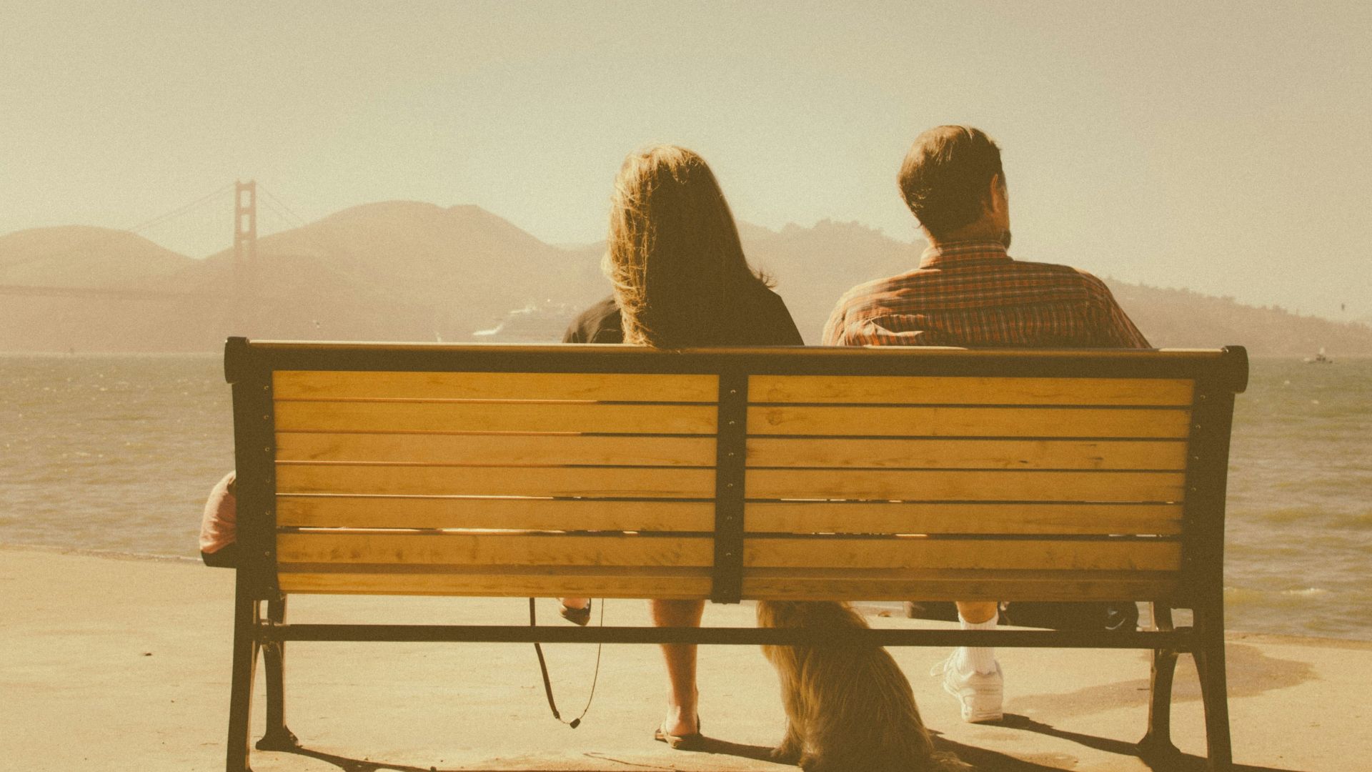 man and woman sitting on bench beside body of water