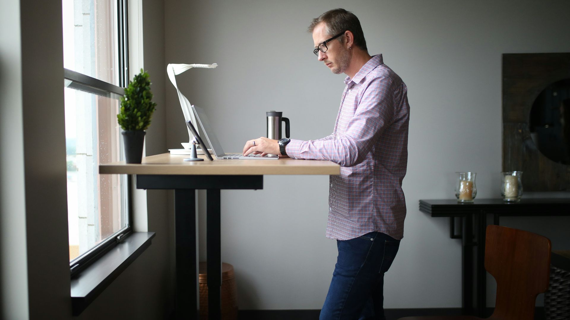 man in pink dress shirt and blue denim jeans standing beside brown wooden table