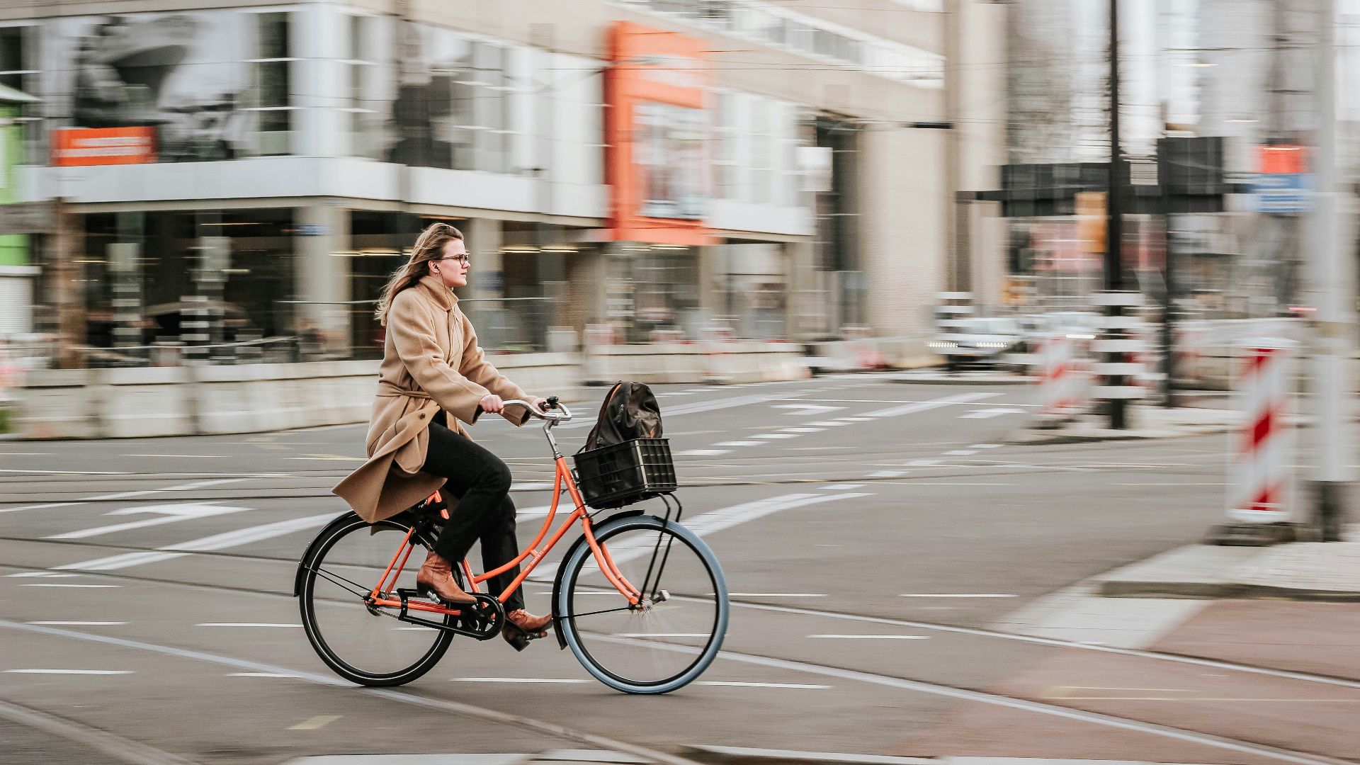 woman in brown coat riding on black bicycle on road during daytime