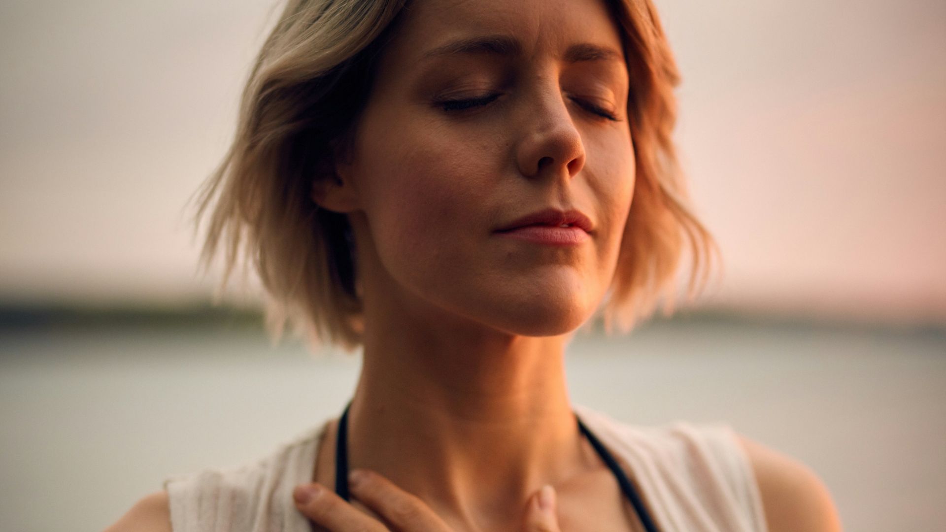 woman in white vest and black bikini with hand on chest