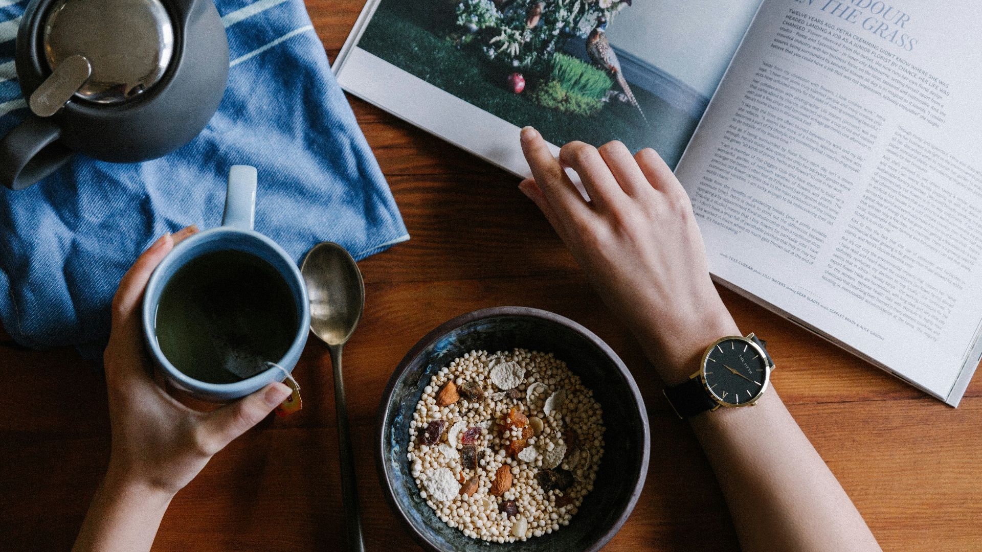 person holding blue ceramic mug and white magazine
